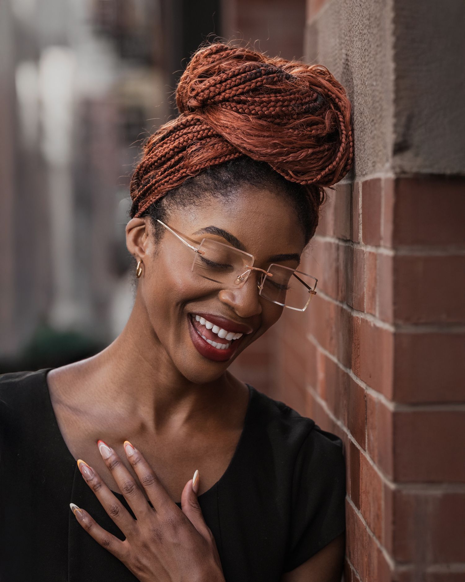 Portrait: candid shot of model laughing with closed eyes, rimless glasses, leaning on brick wall, natural cinematic light.