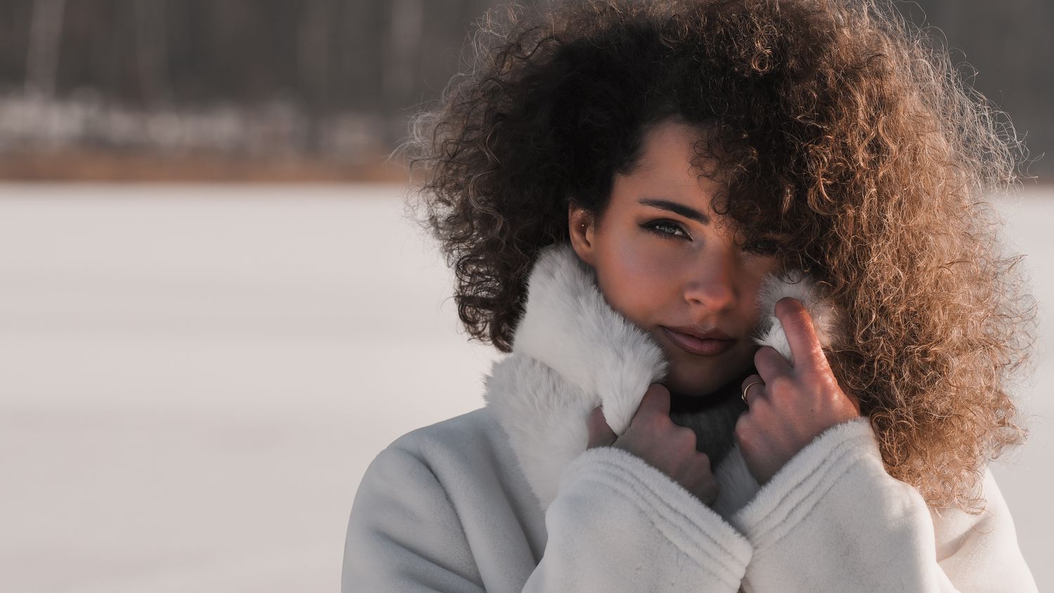 Professional winter fashion portrait: model with curly hair snuggling into a fur collar, white sheepskin coat, intense look at the camera.