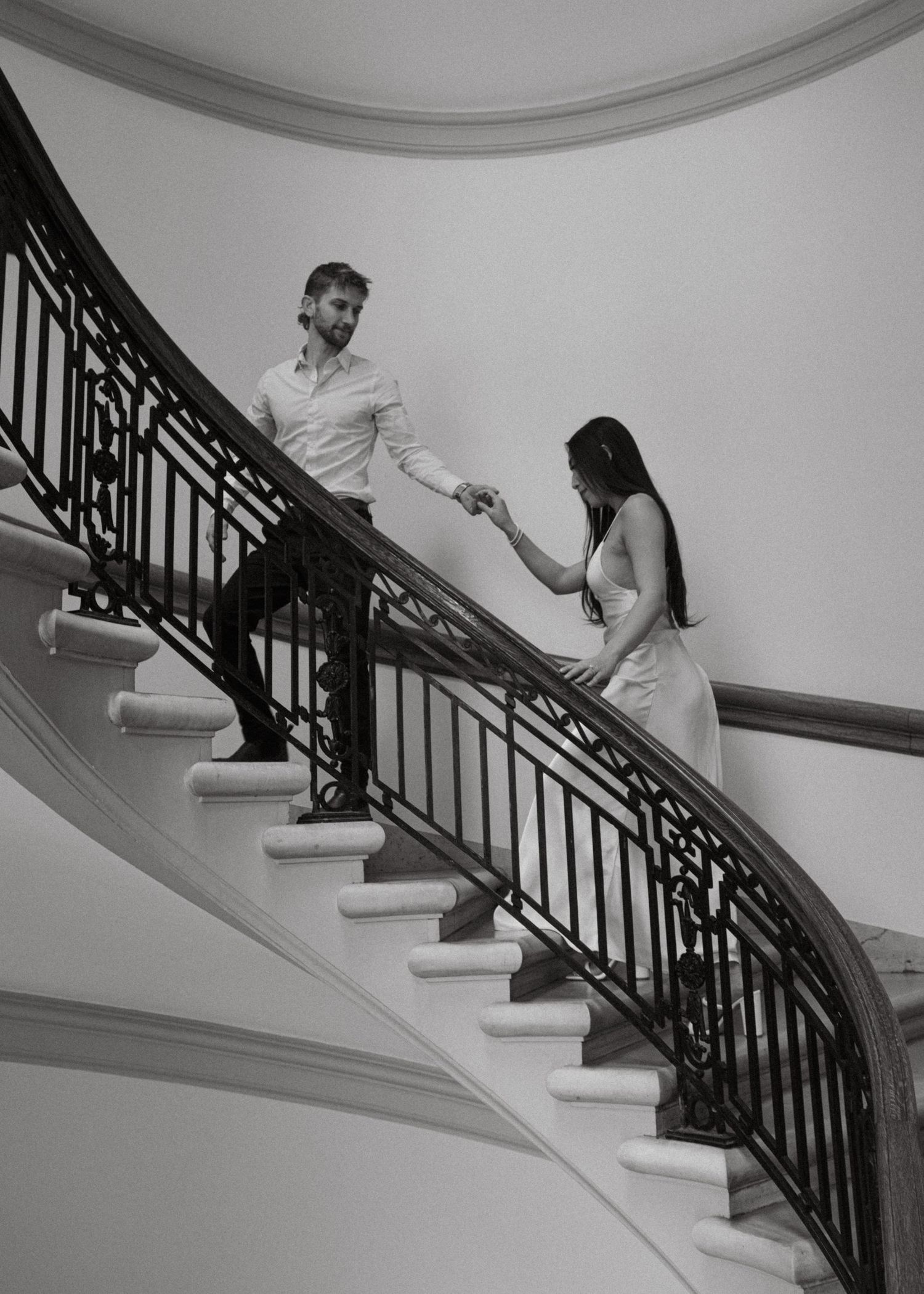 A sequence of black and white photos showing two people playfully sliding down an elegant curved staircase banister.