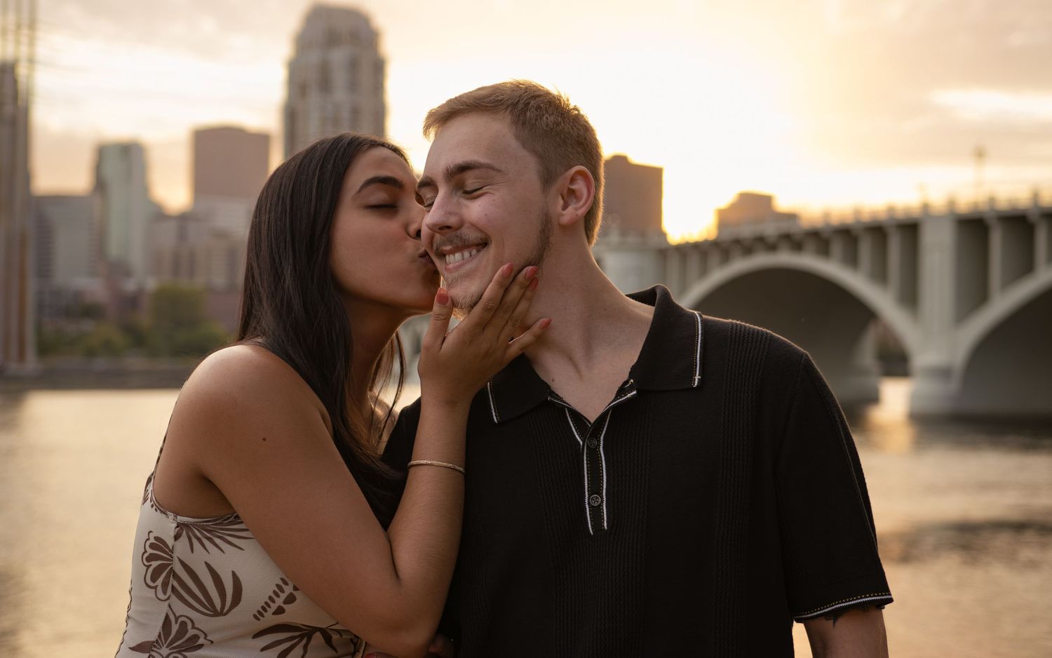 Romantic couple moment captured during sunset with city backdrop.