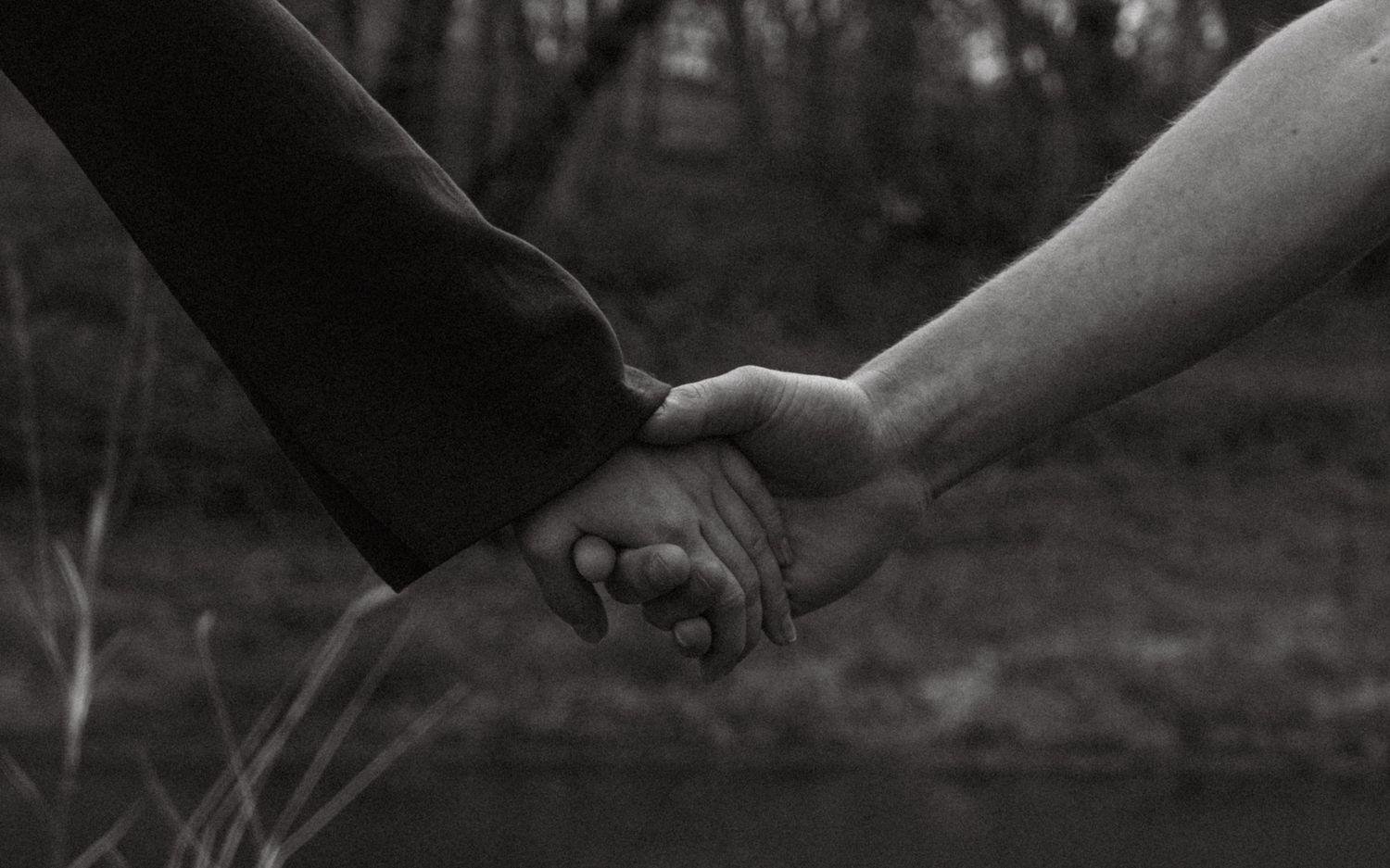 Black and white photo of two people holding hands outdoors, symbolizing love and connection.