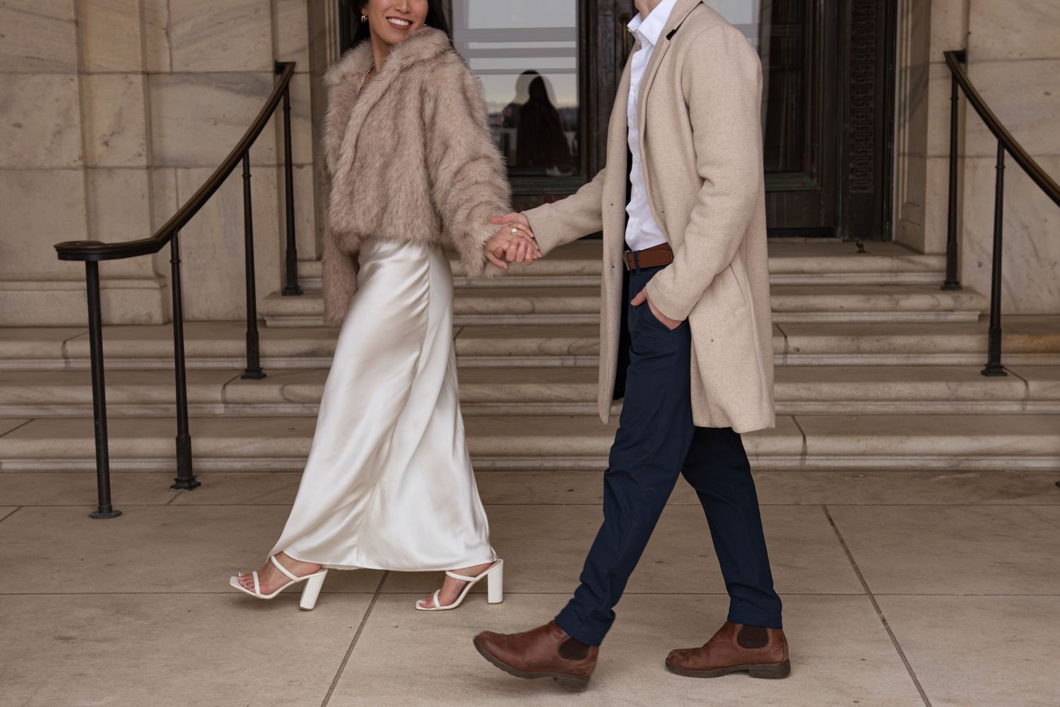 A couple walks together through an elegant stone archway in formal attire during a special occasion.