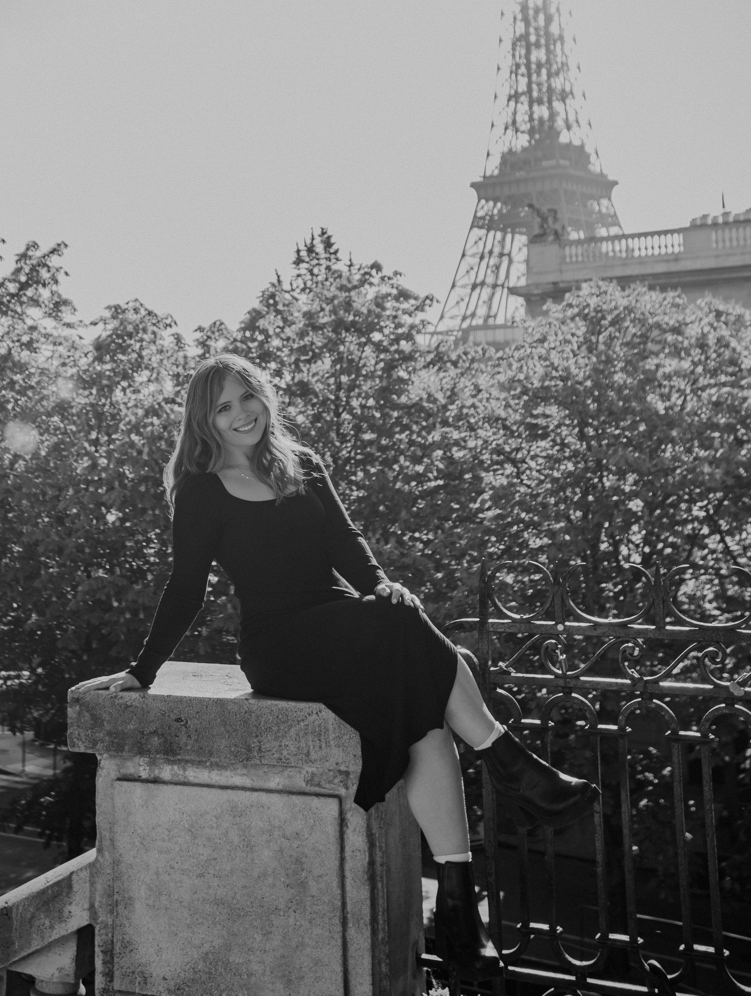 Woman in black dress sitting on stone wall with Eiffel Tower visible in Paris.