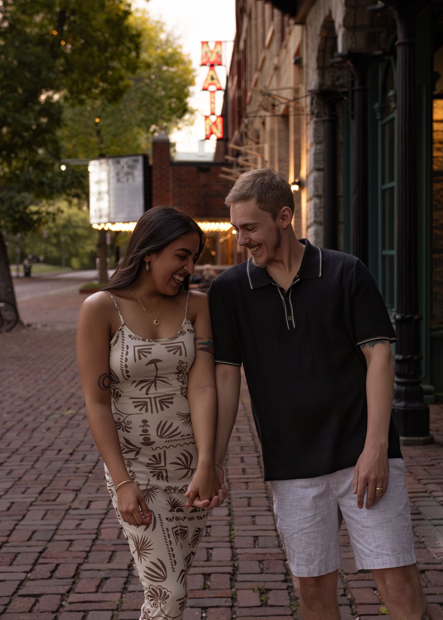 A couple walks and laughs together on a brick sidewalk during an evening photoshoot.