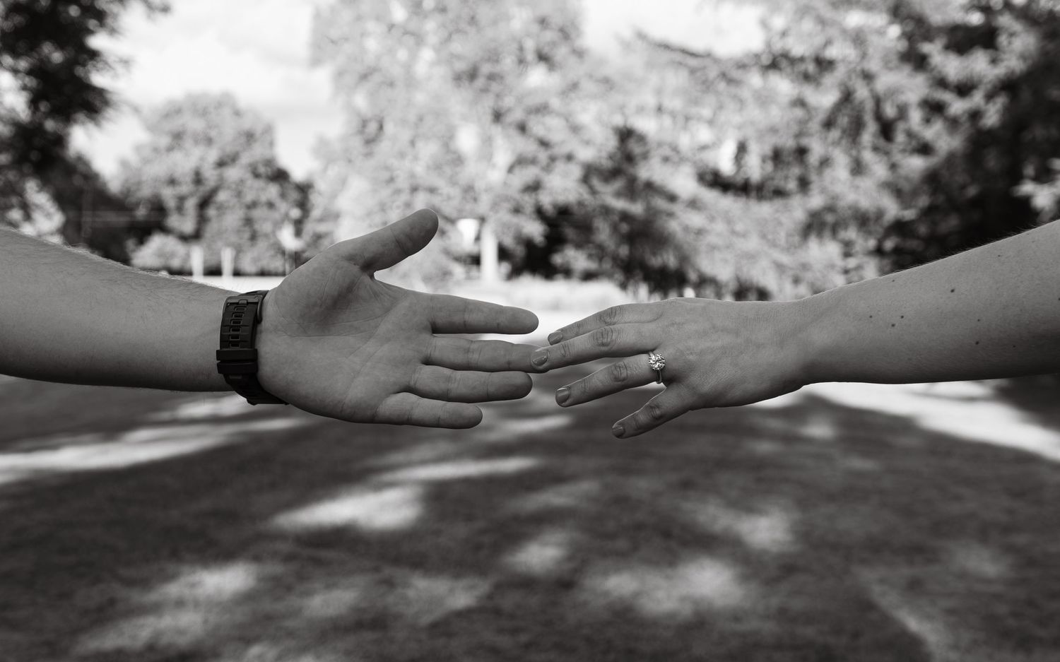 Two hands reaching toward each other in a black and white outdoor photo, symbolizing connection and togetherness.
