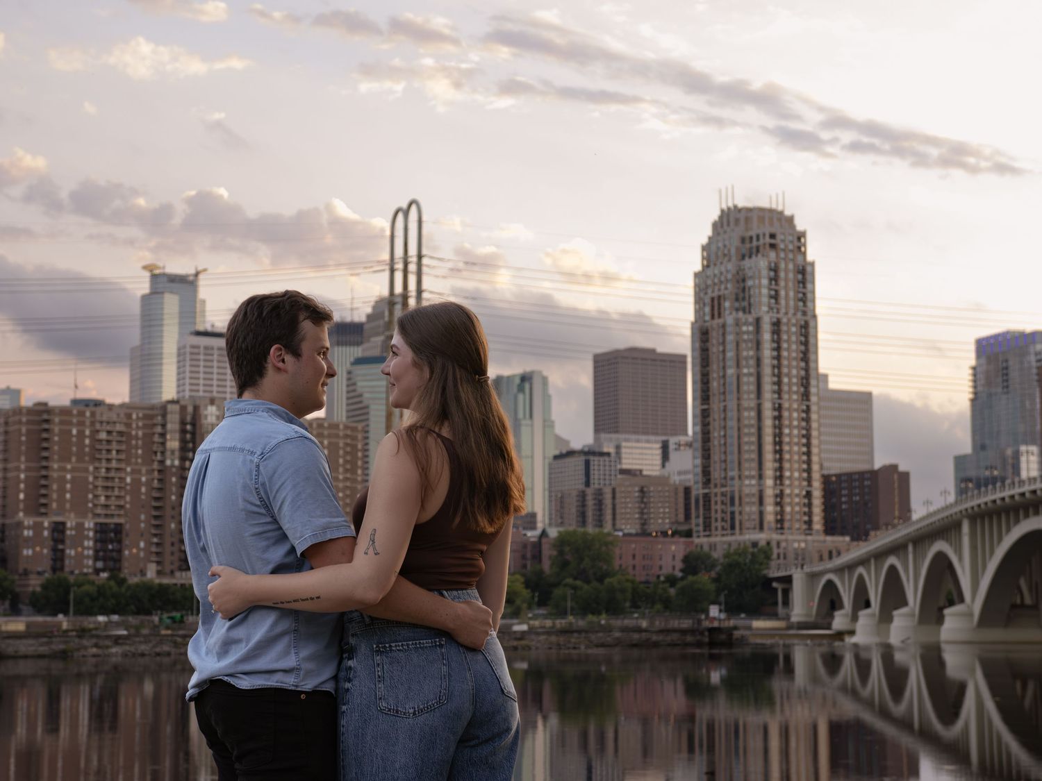 Romantic couple embracing at sunset with urban skyline and bridge in the background.
