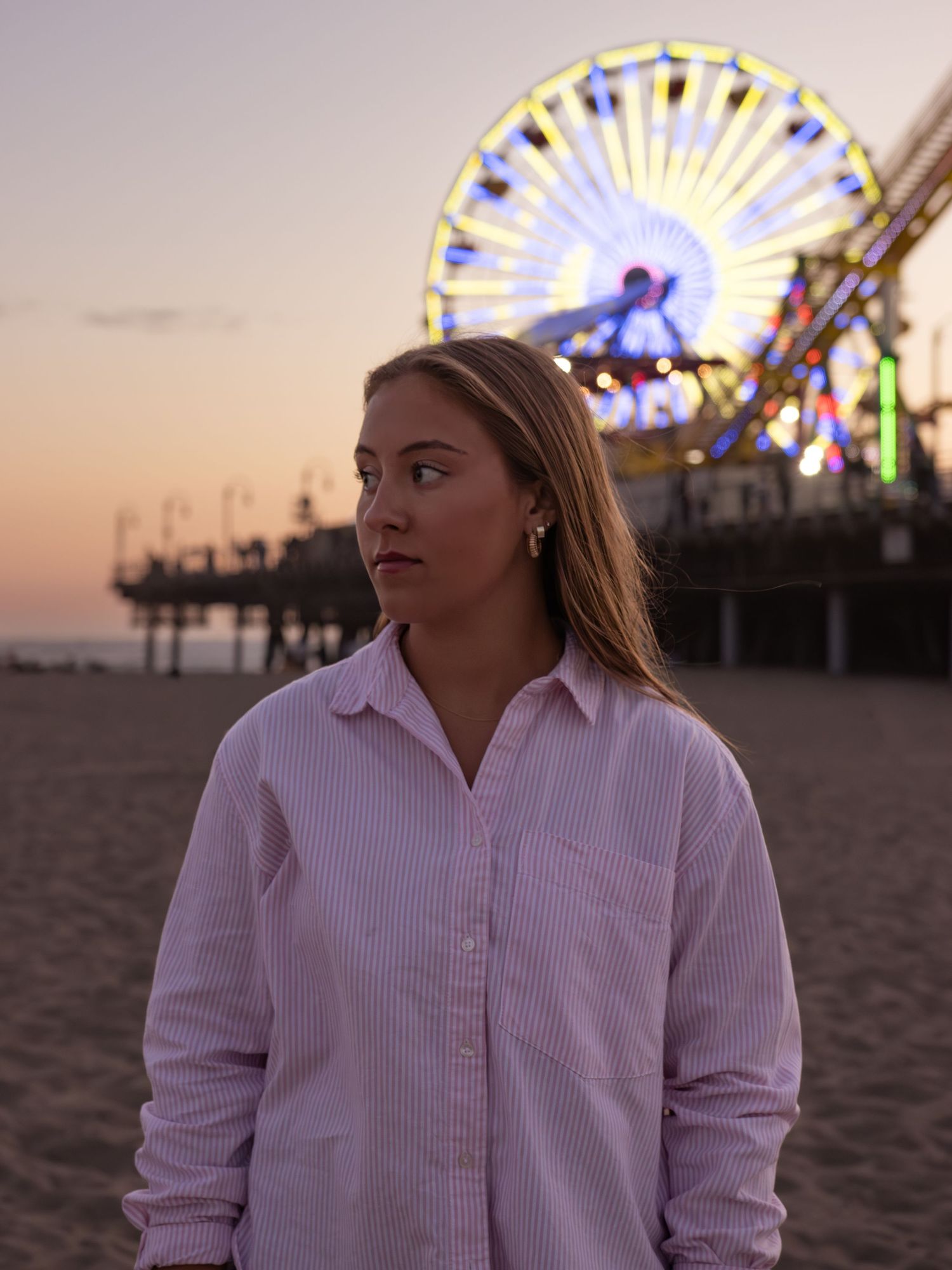 Person in white shirt sitting on beach with amusement park pier in background.