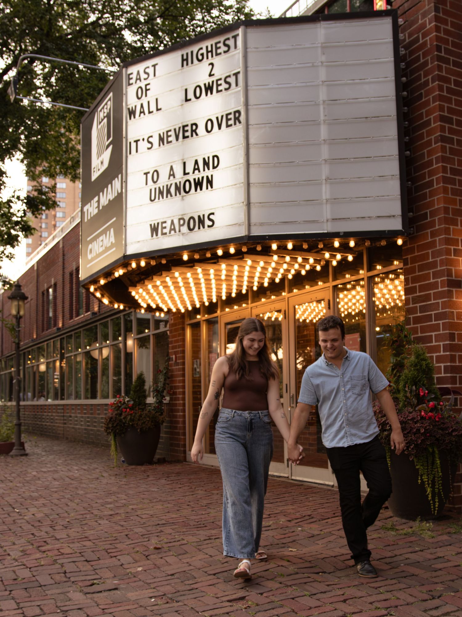 Couple walking together under illuminated theater marquee lights at dusk.