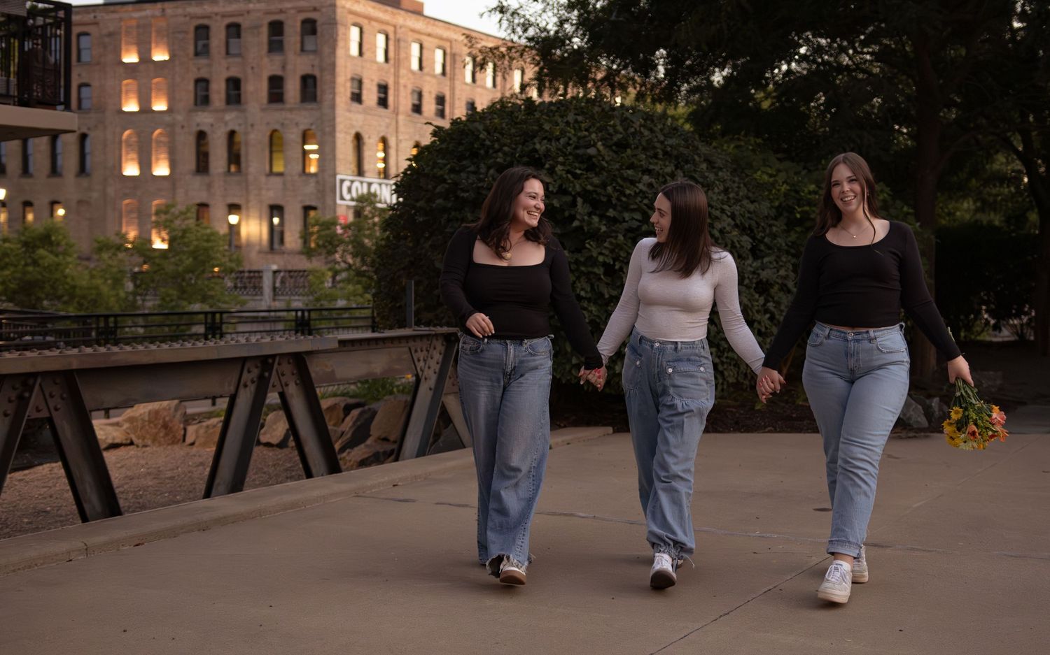Three people walking together on a paved path near brick buildings at dusk.