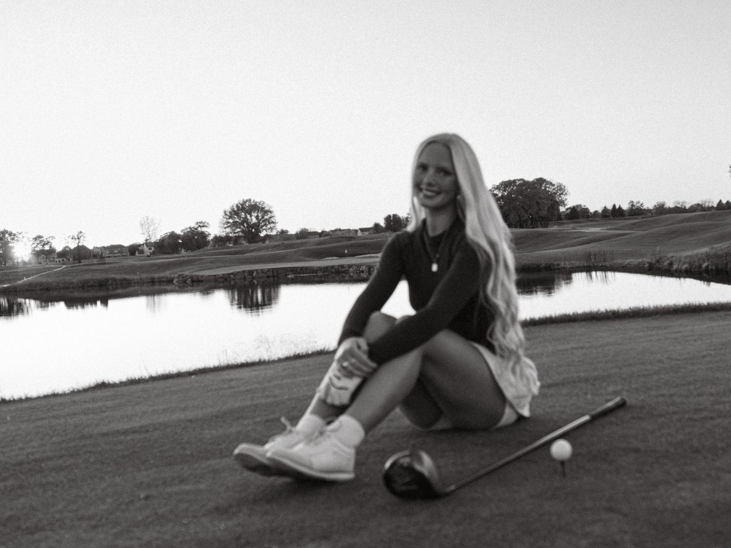 Black and white photo of golf course scenery with person relaxing near water.