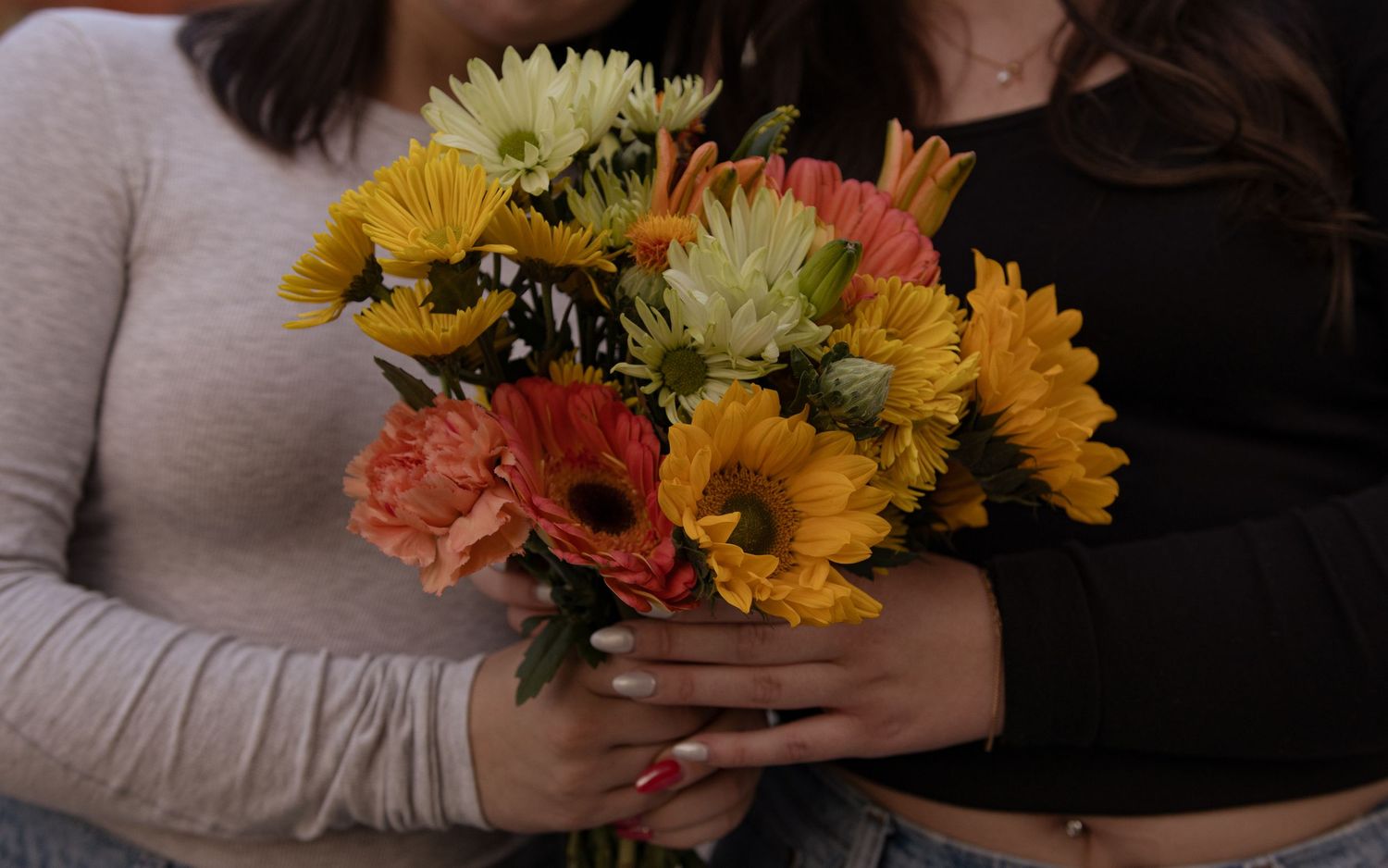 Person holding a vibrant bouquet of sunflowers and mixed flowers.
