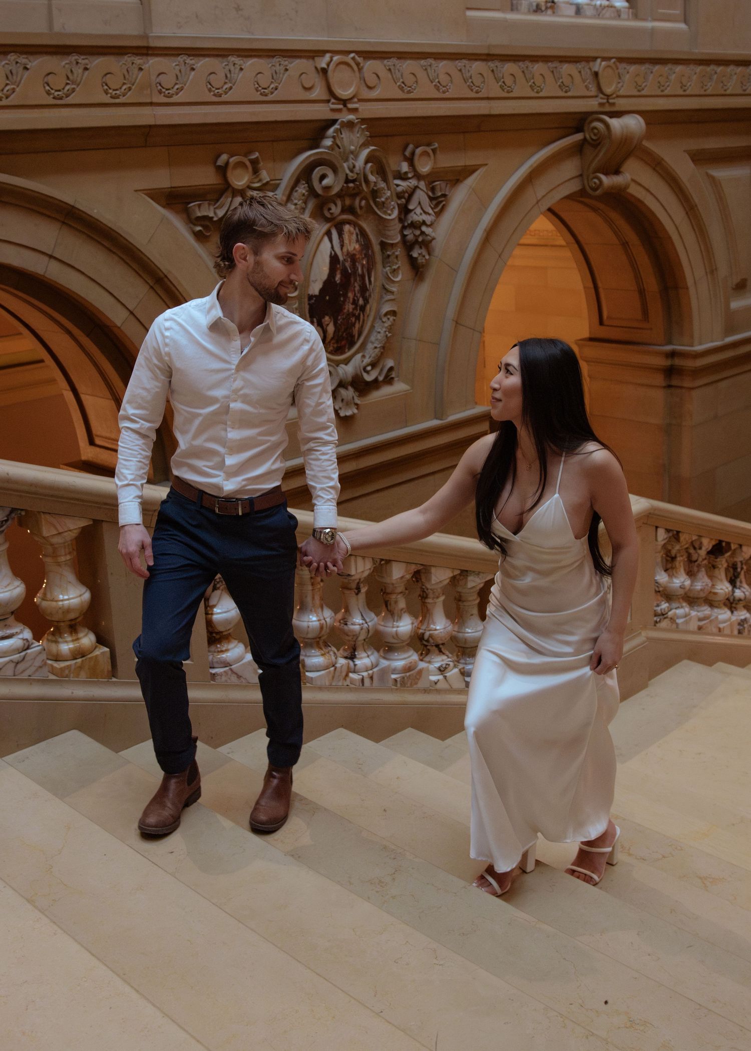 Couple sitting and talking on elegant marble stairs in a historic building with ornate architectural details.