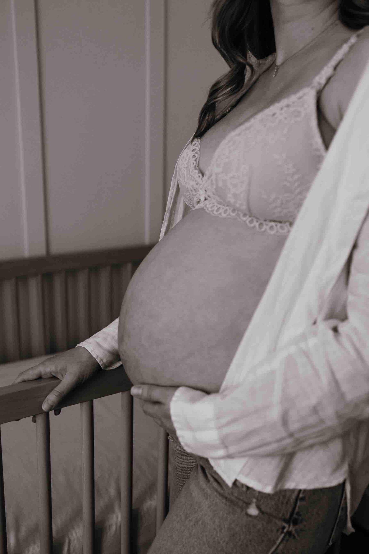 Close-up of an expectant mother's baby bump beside the nursery crib, celebrating anticipation and motherhood in Toronto.