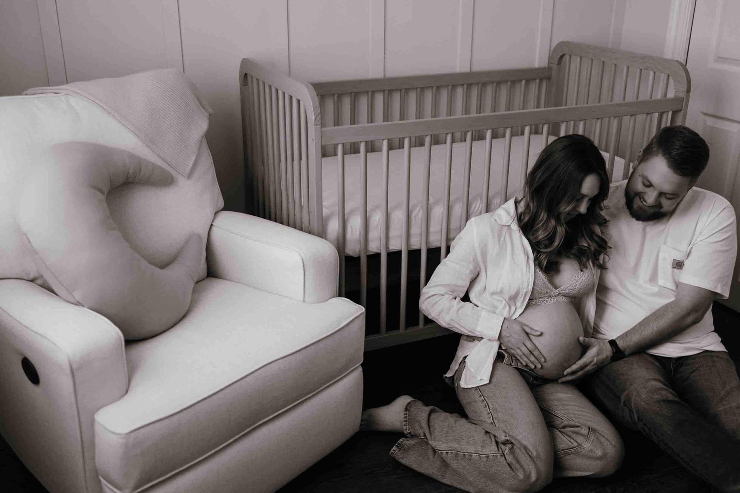 Expectant parents admiring their baby bump beside the nursery crib during an in-home maternity photography session in Toronto.