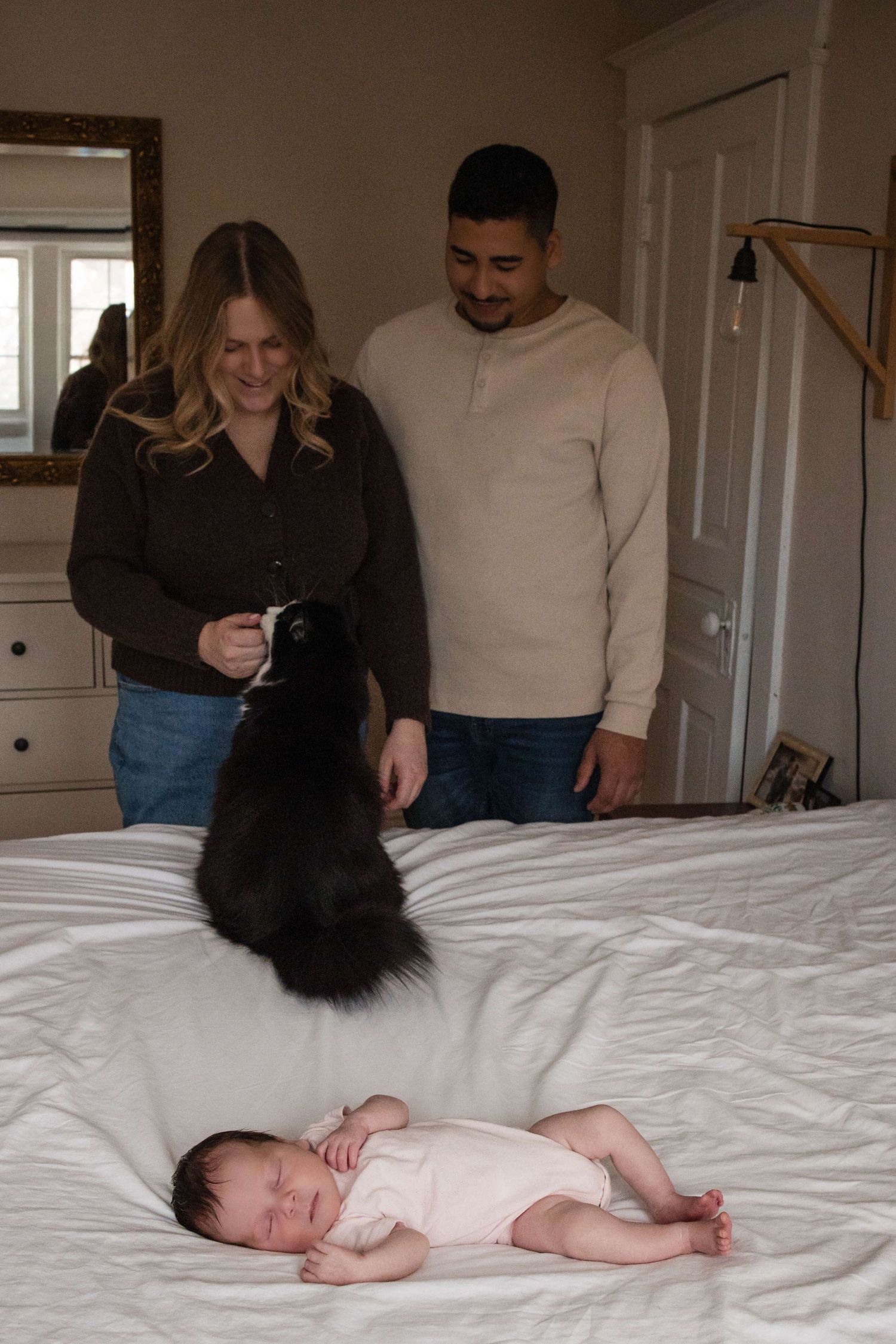 Parents, newborn, and family cat sharing a quiet moment during an in-home newborn photography session in Toronto, capturing real family life
