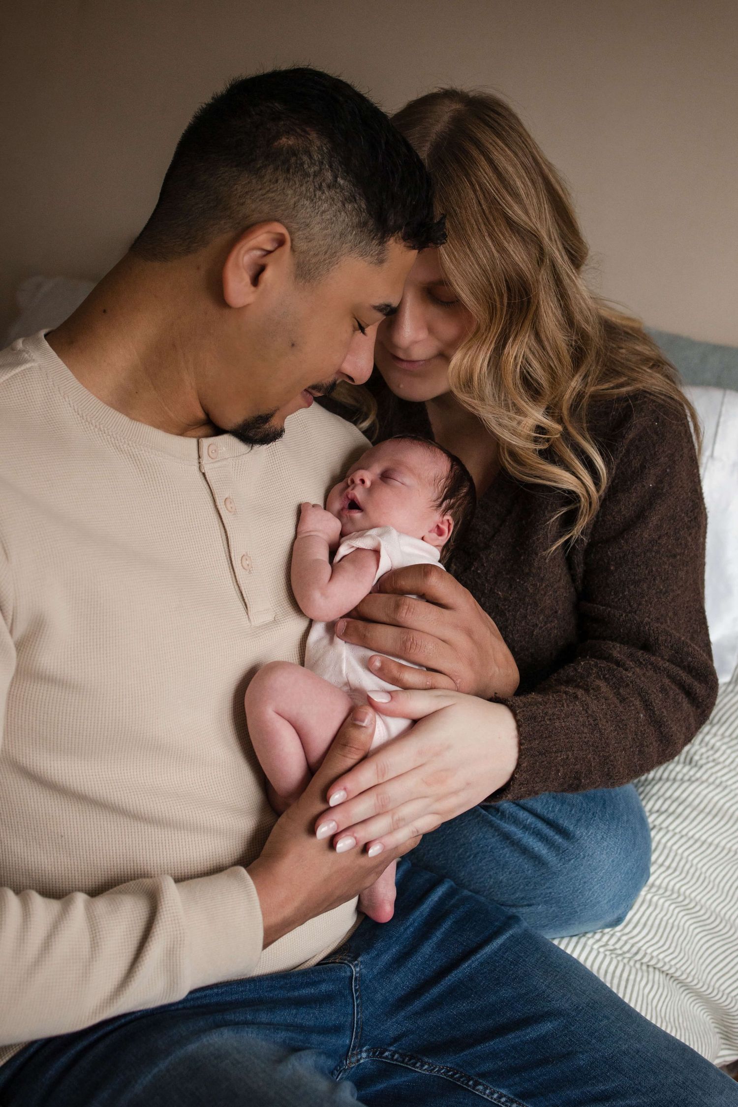 Parents cuddling their newborn during an in-home newborn photography session in Toronto, capturing love, connection, and family.
