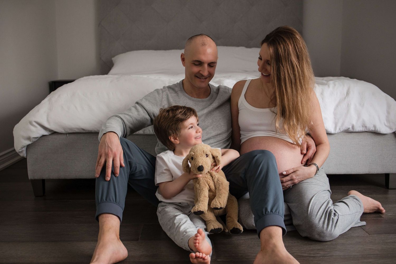 Expectant parents and their child sharing a cozy family moment during an in-home maternity photography session in Toronto.