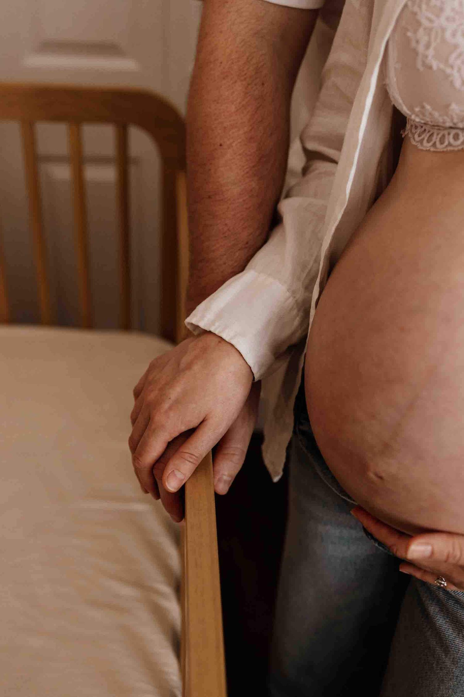 Close-up of expectant parents' hands beside the nursery crib during an in-home maternity photography session in Toronto.