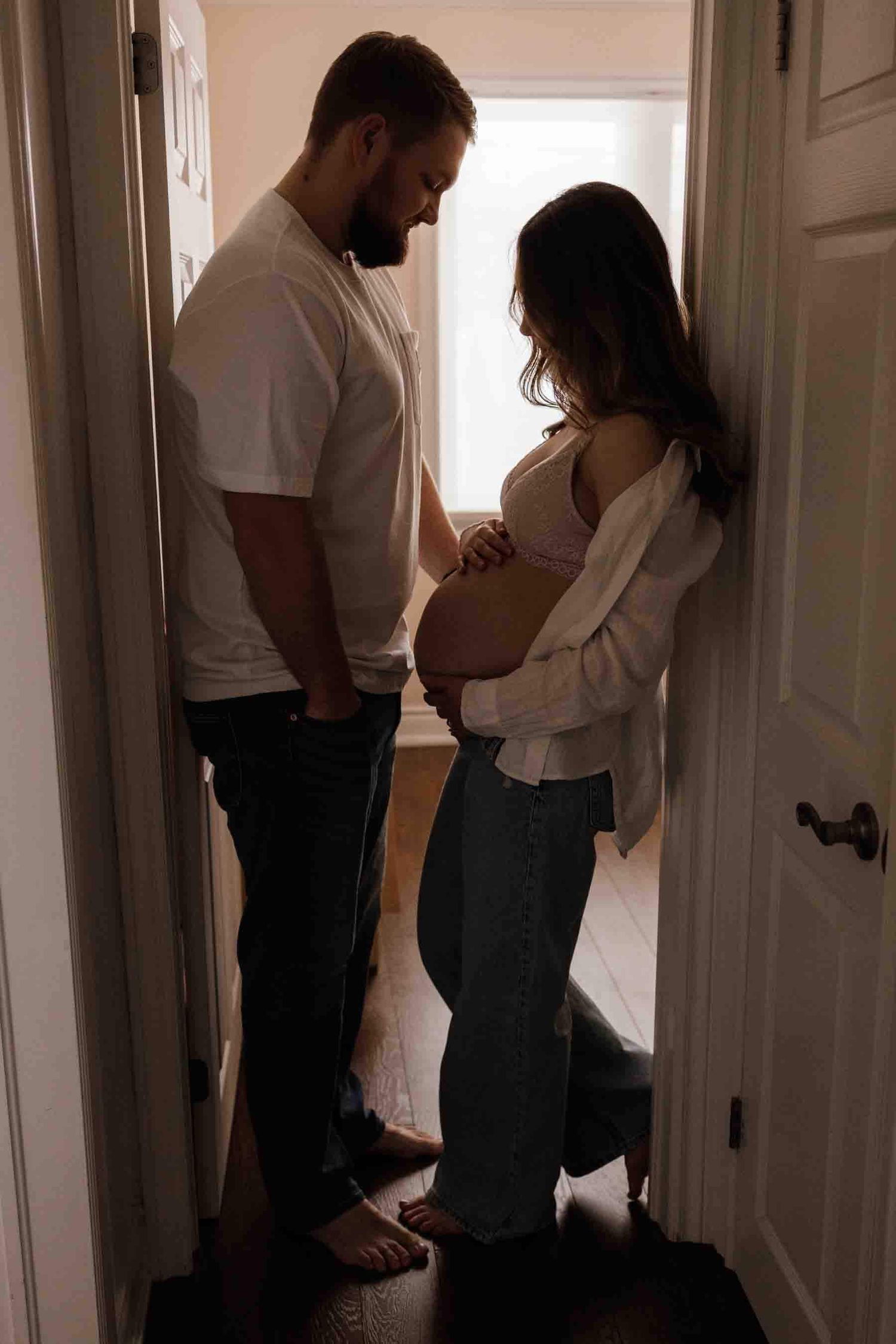 Expectant parents sharing a quiet moment in a doorway during an in-home maternity photography session in Toronto, celebrating anticipation.