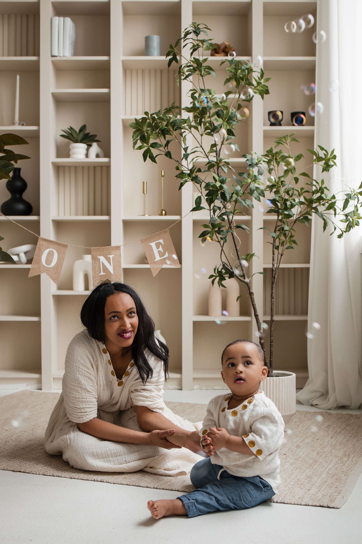 Mother and one-year-old enjoying playful moments during a cake smash session at Mint Room Studios in Toronto with bubbles and neutral decor.