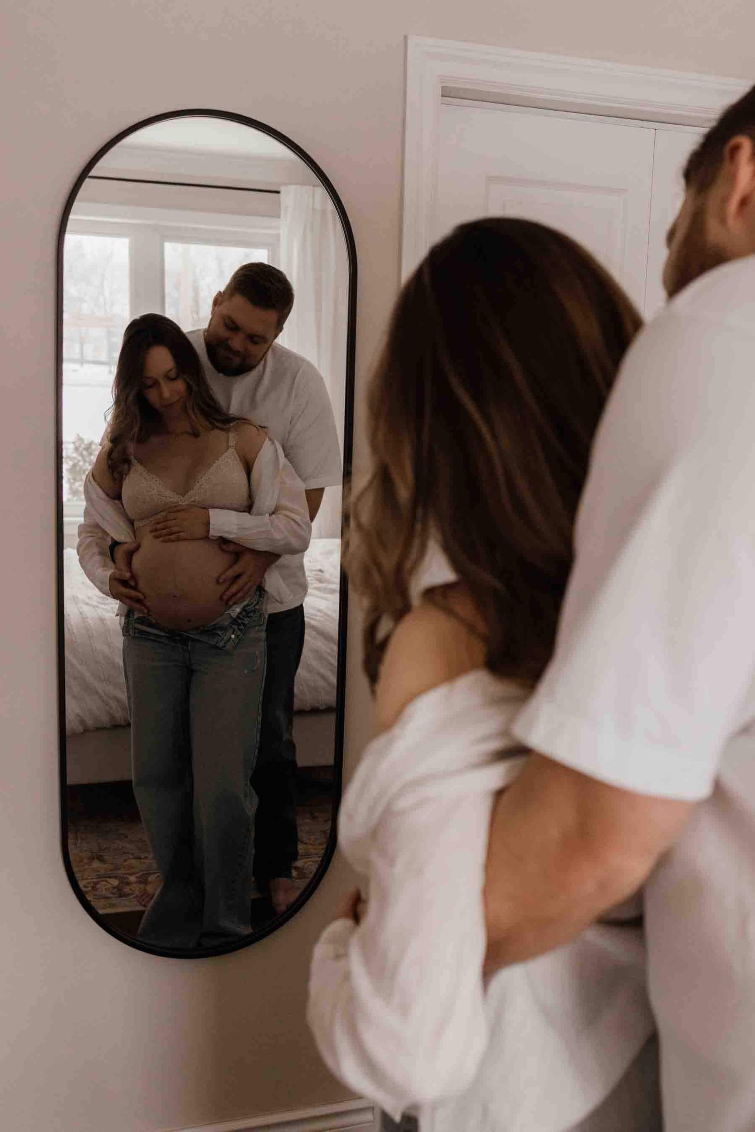 Expectant parents embracing in a mirror reflection during an in-home maternity photography session in Toronto, celebrating anticipation.