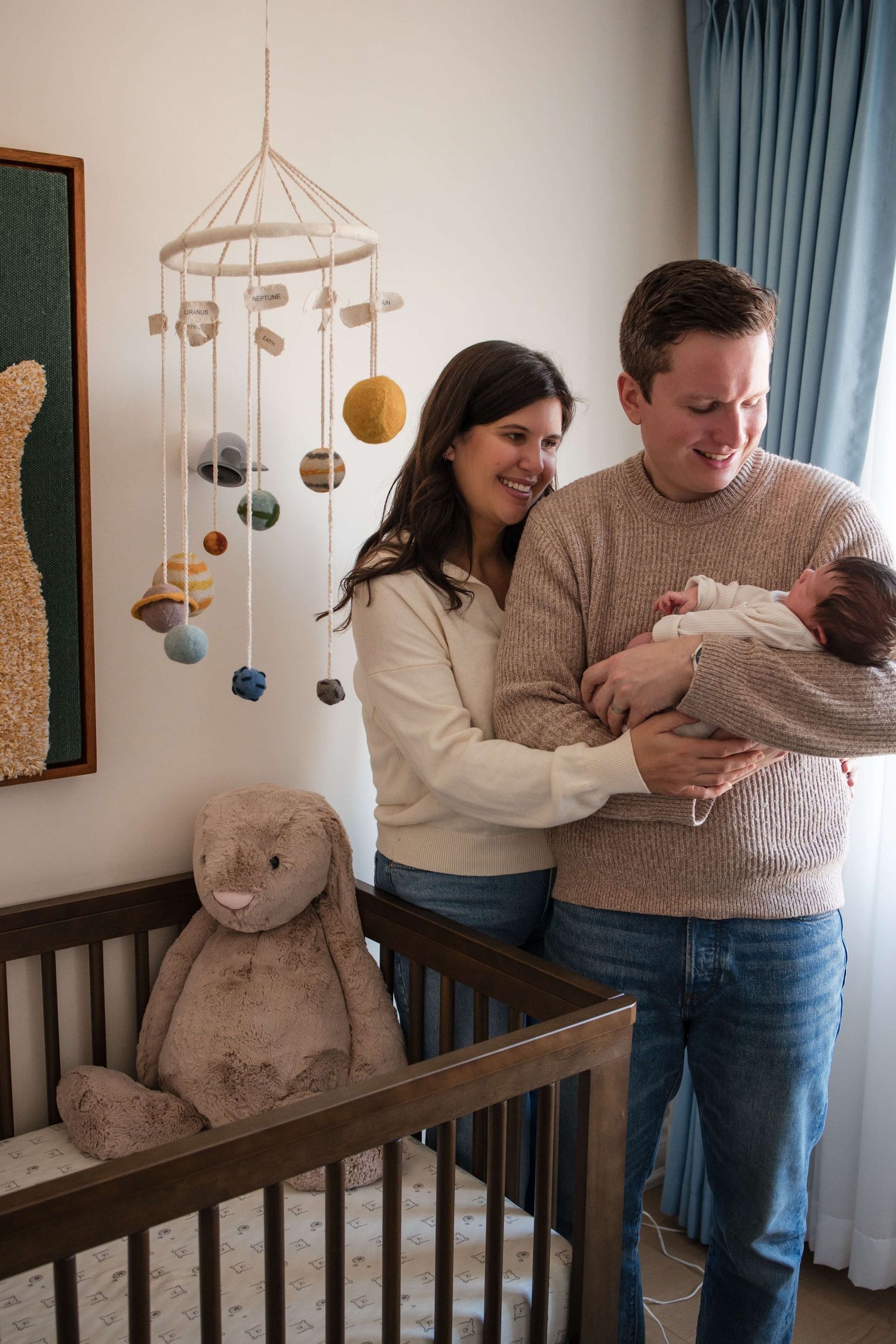 Father holding his newborn while parents share a joyful moment in the nursery during a Toronto newborn session.