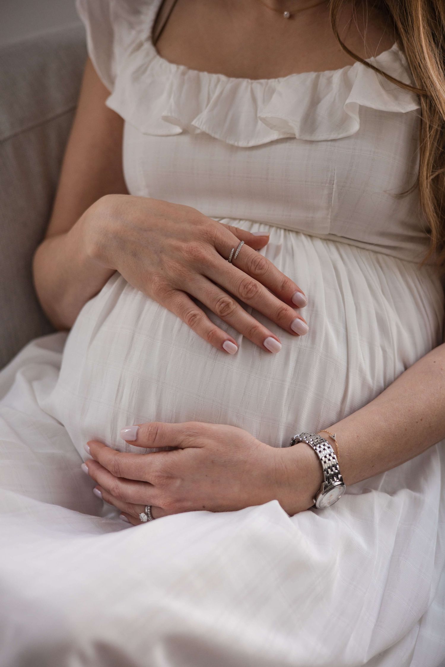 Close-up of an expectant mother’s hands resting on her baby bump during an in-home maternity photography session in Toronto.