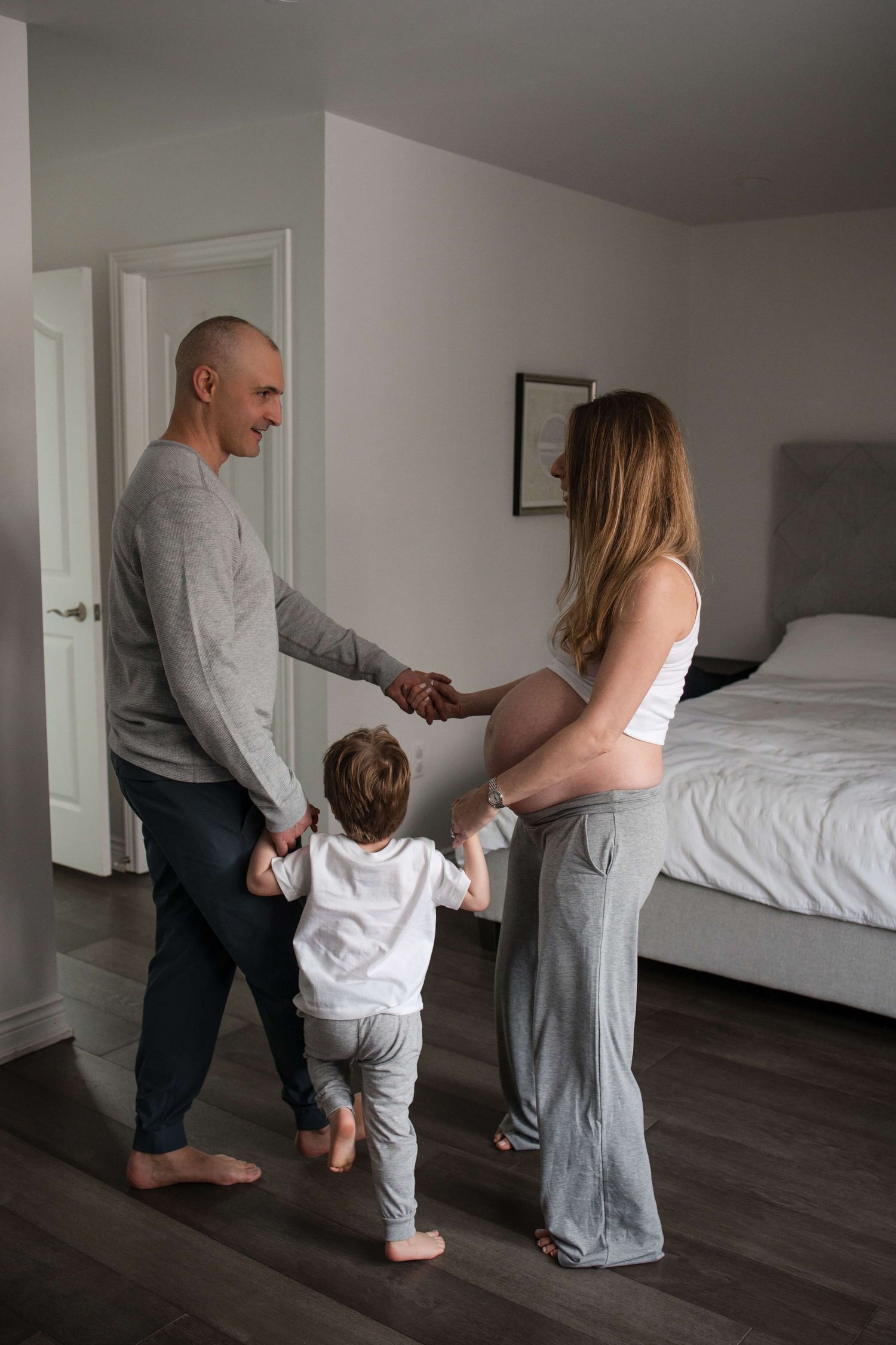 Expectant parents and their child walking together during an in-home maternity photography session in Toronto, celebrating a growing family.