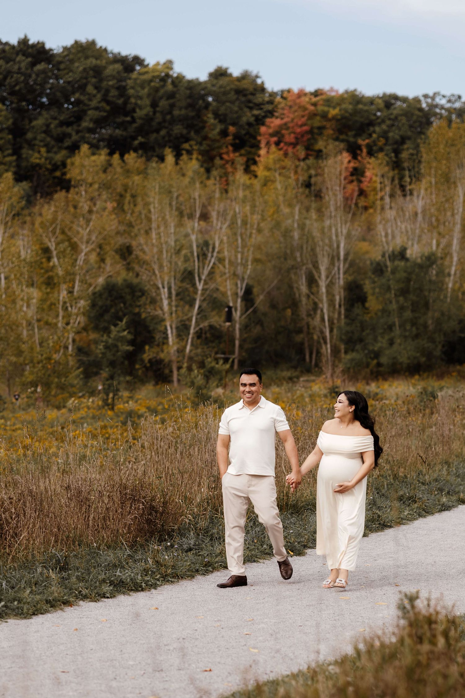 Expectant parents walking hand in hand during an autumn outdoor maternity photography session at Evergreen Brick Works in Toronto.