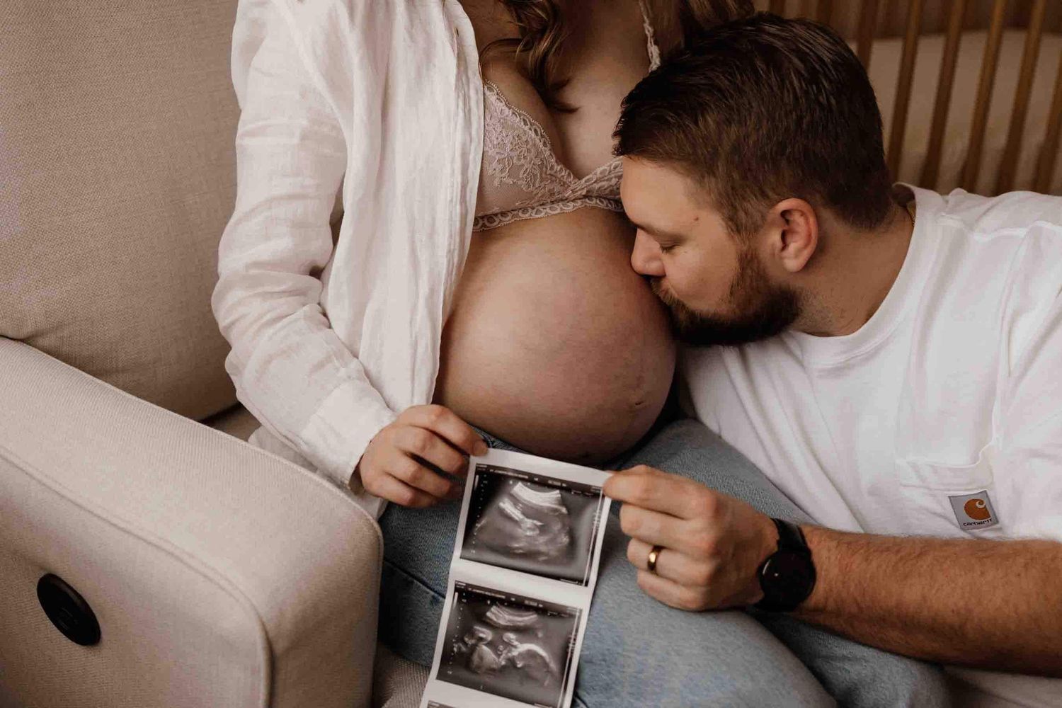 Father kissing an expectant mother's baby bump while holding ultrasound photos during a maternity photography session in Toronto.