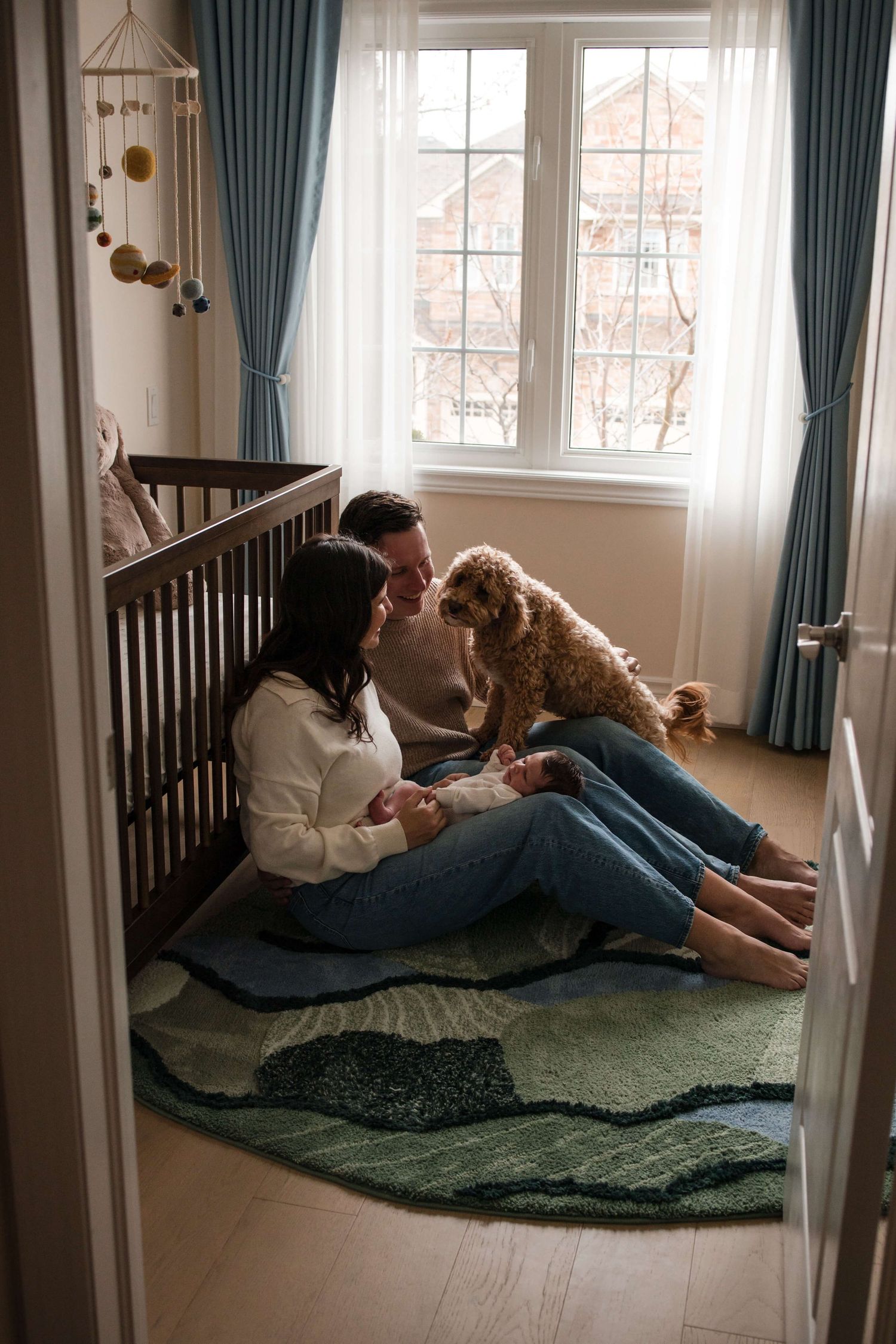 Parents, newborn, and family dog sharing a peaceful moment in the nursery during a Toronto newborn session.