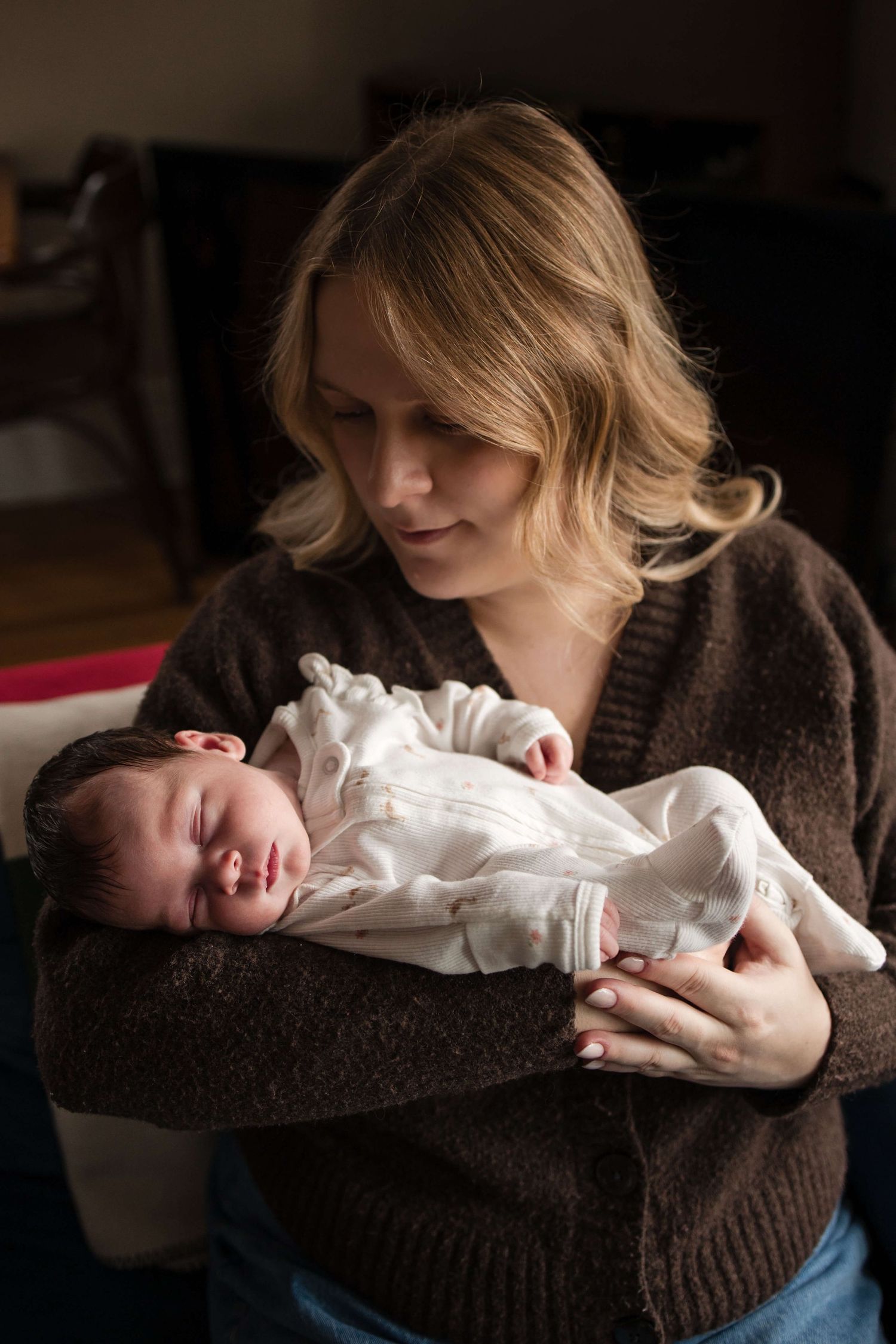 Mother holding her sleeping newborn during an in-home newborn photography session in Toronto, capturing tenderness, love, and connection.