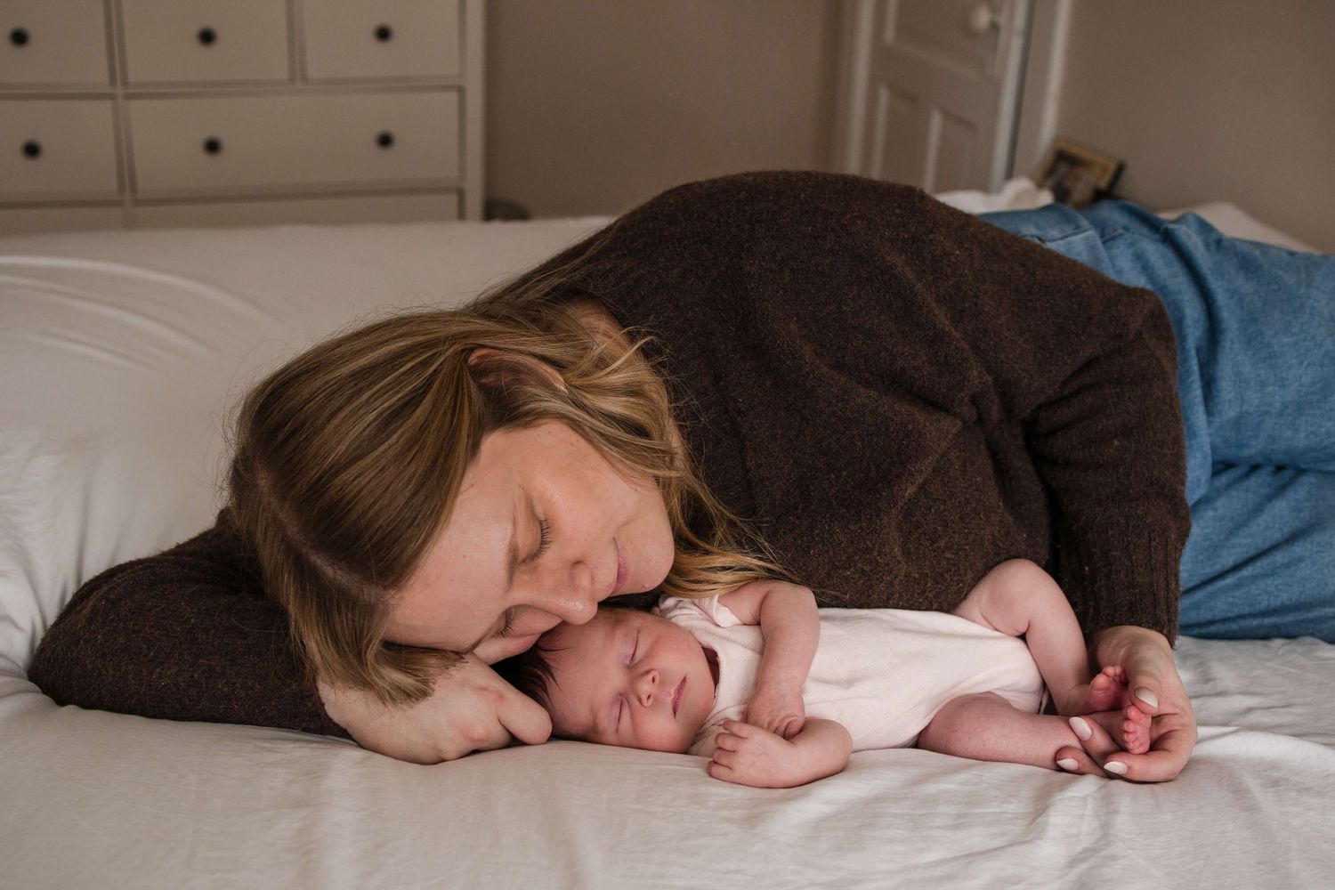 Mother cuddling her newborn on the bed during an in-home newborn photography session in Toronto, capturing love, comfort, and connection.