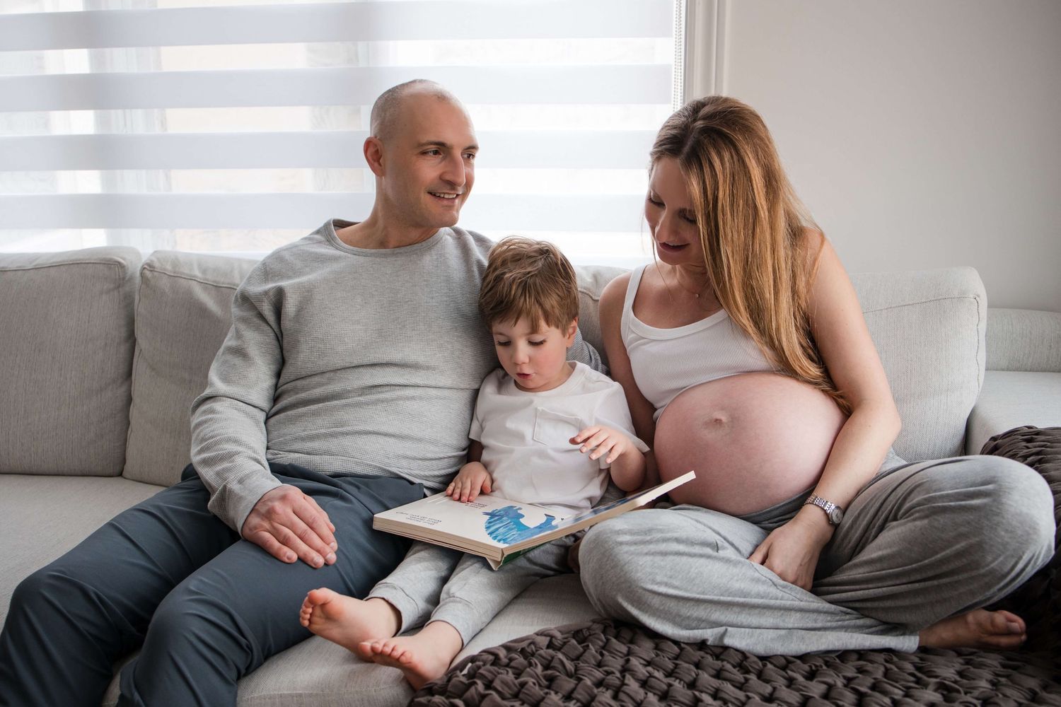 Expectant parents reading with their child during an in-home maternity photography session in Toronto, celebrating family and anticipation.