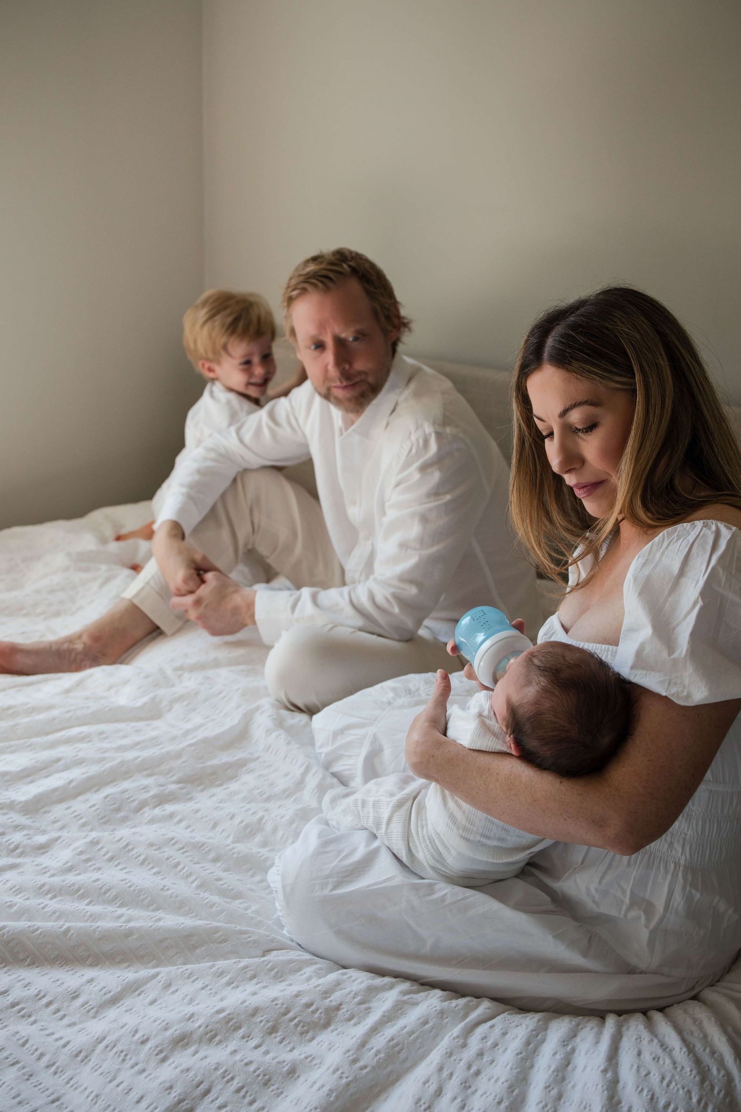 Mother feeding her newborn while surrounded by family during a relaxed in-home newborn session in Toronto.