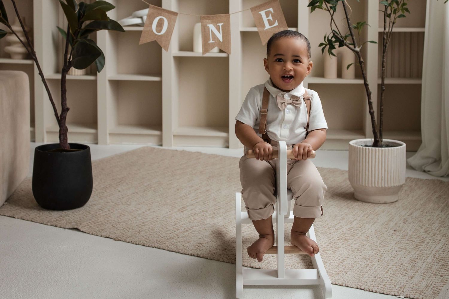 One-year-old sitting on a wooden stool during a cake smash session at Mint Room Studios in Toronto with timeless neutral decor.