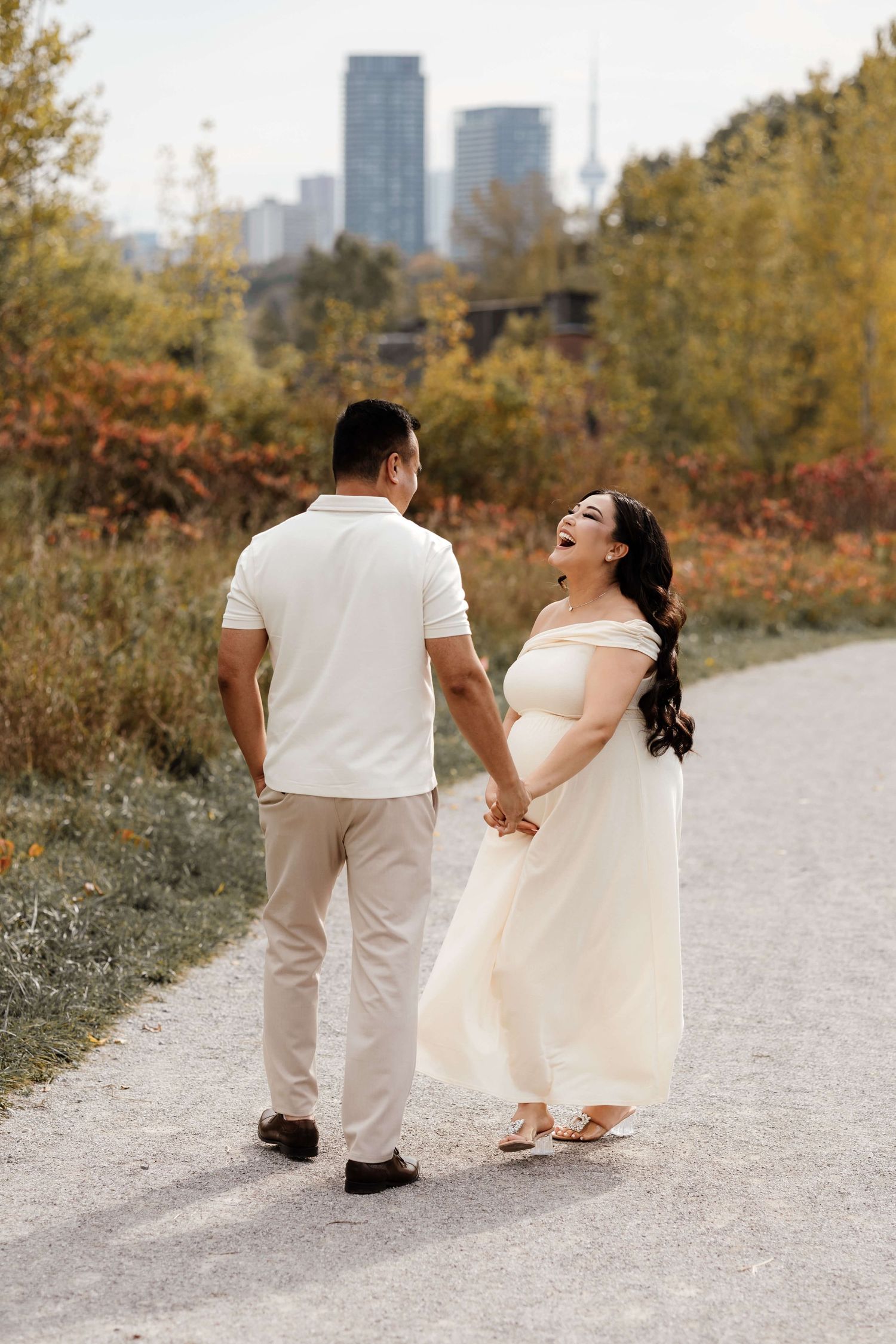 Expectant parents sharing a joyful moment at Evergreen Brick Works with the CN Tower in the background during maternity session in Toronto.