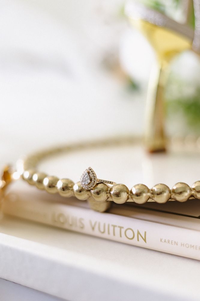Elegant wedding details including a Louis Vuitton accessory, pearl necklace, and diamond ring on white surface.