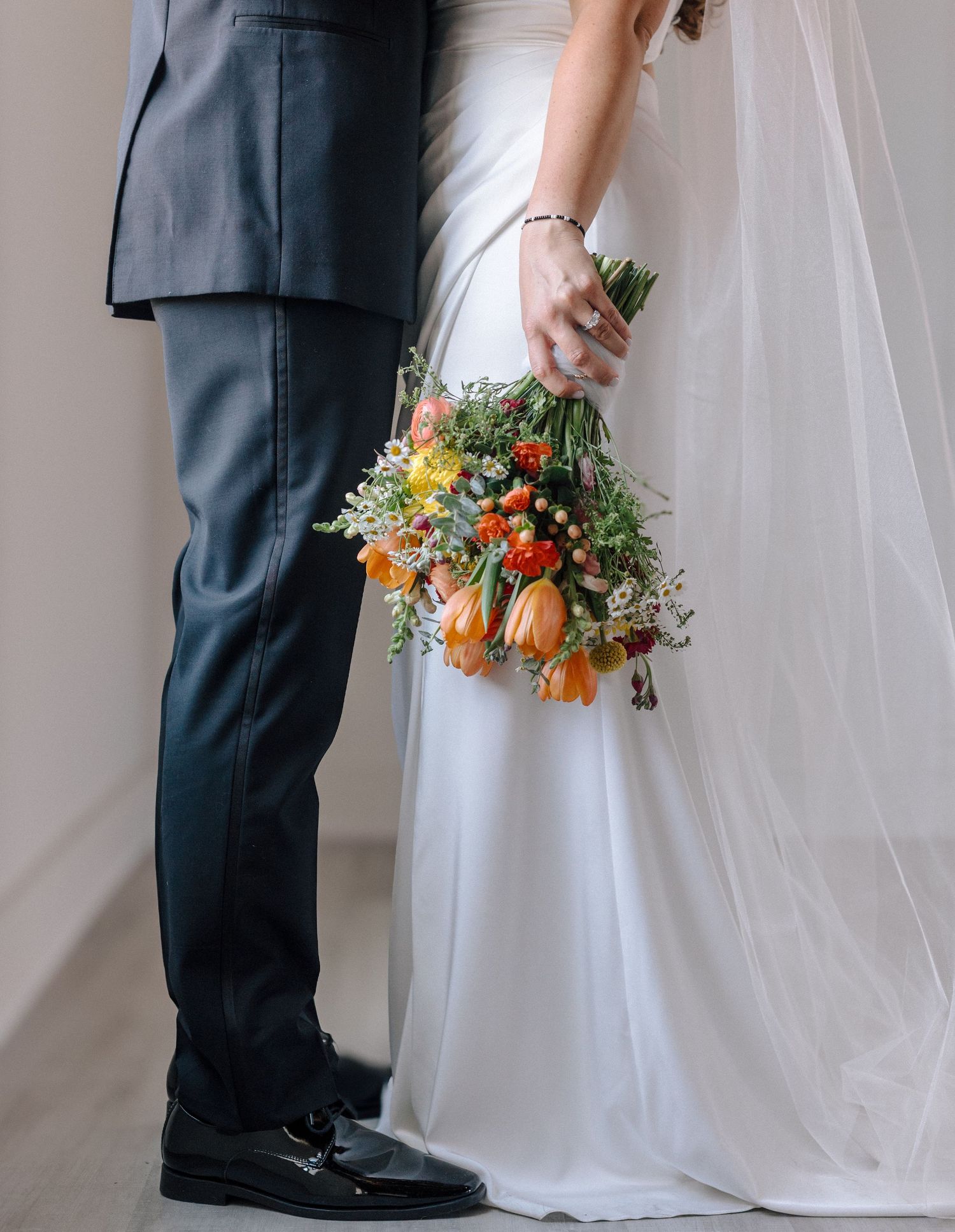 Wedding detail shot showing formal attire and colorful bouquet against neutral background.