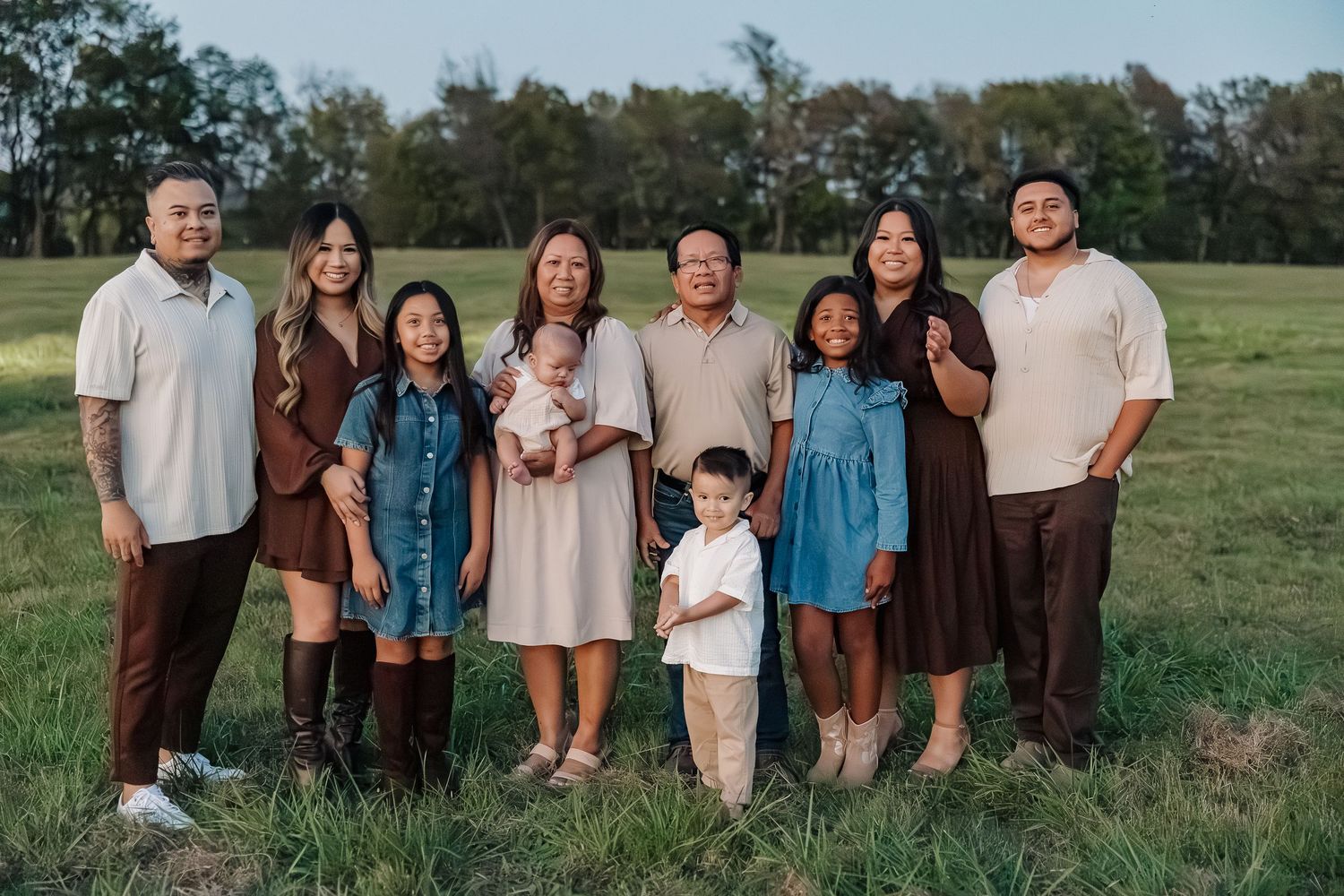 Family group portrait in earth-toned clothing standing together in a field at sunset.