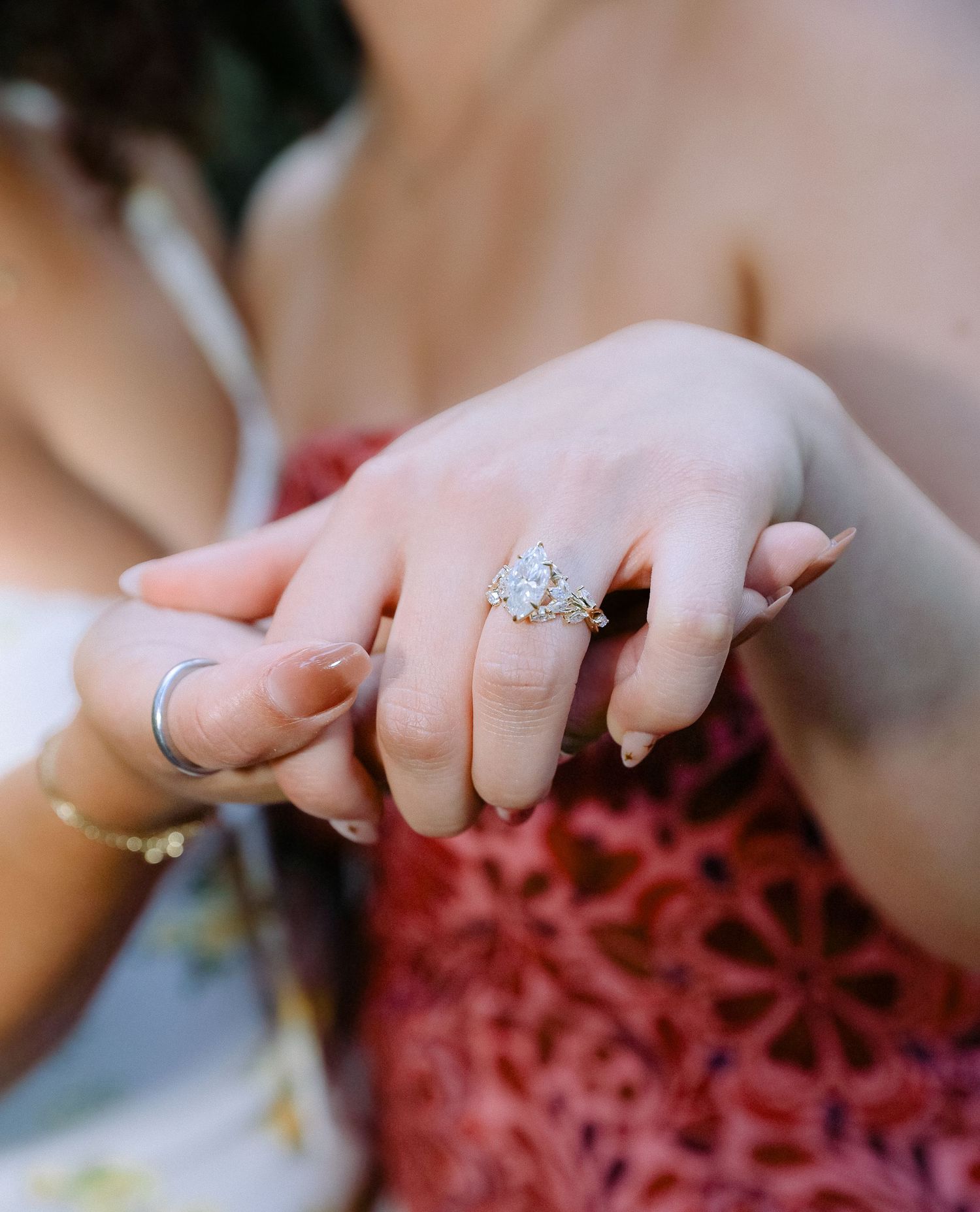 Close-up of hands wearing diamond engagement rings and wedding bands against a red floral background.