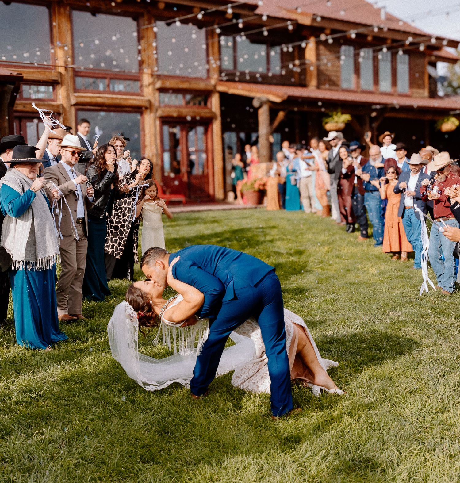Wedding guests participate in a fun lawn game at an outdoor reception venue with wooden beams and string lights.