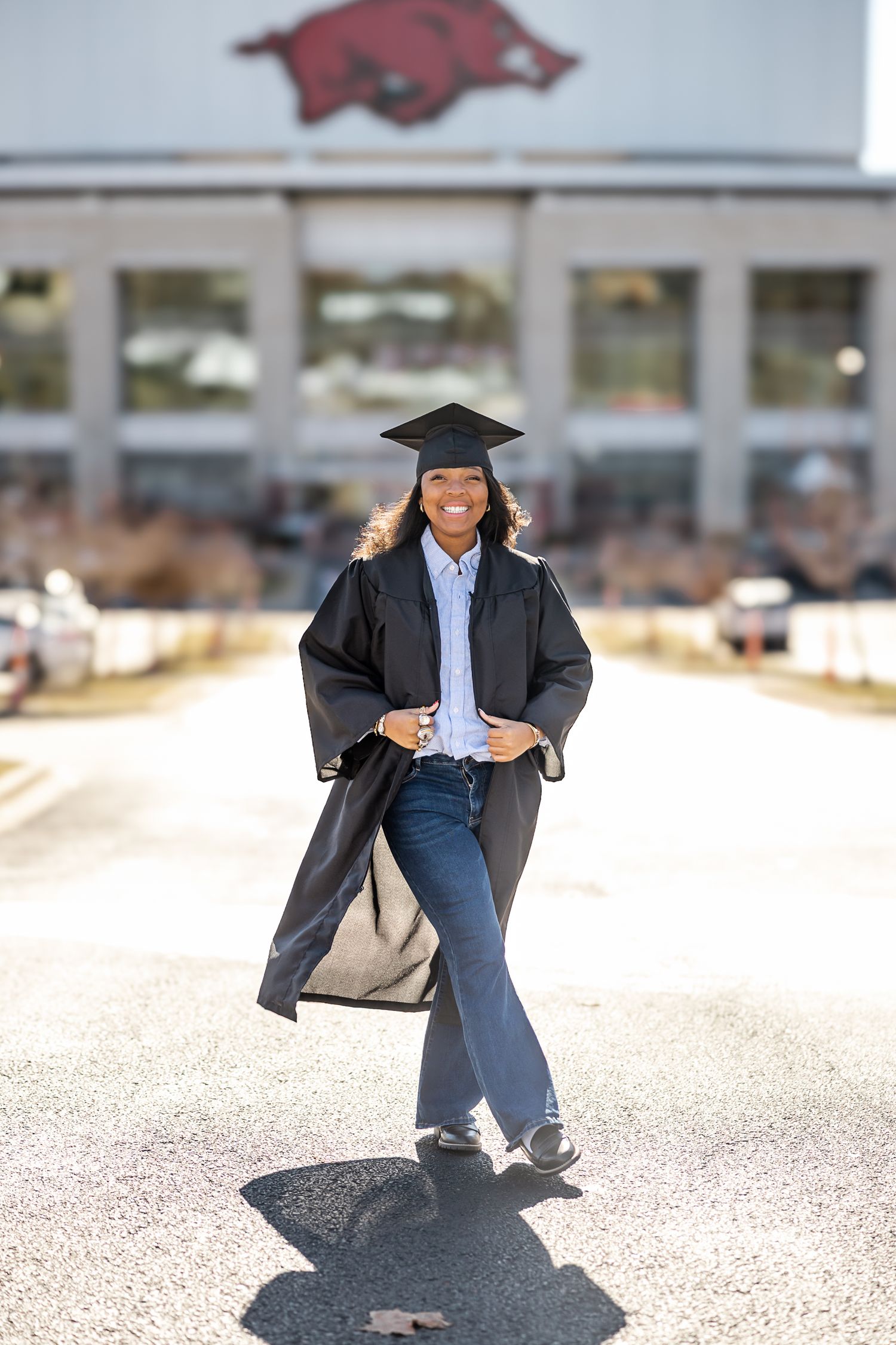 Graduate in cap and gown poses for creative photo series on outdoor path.