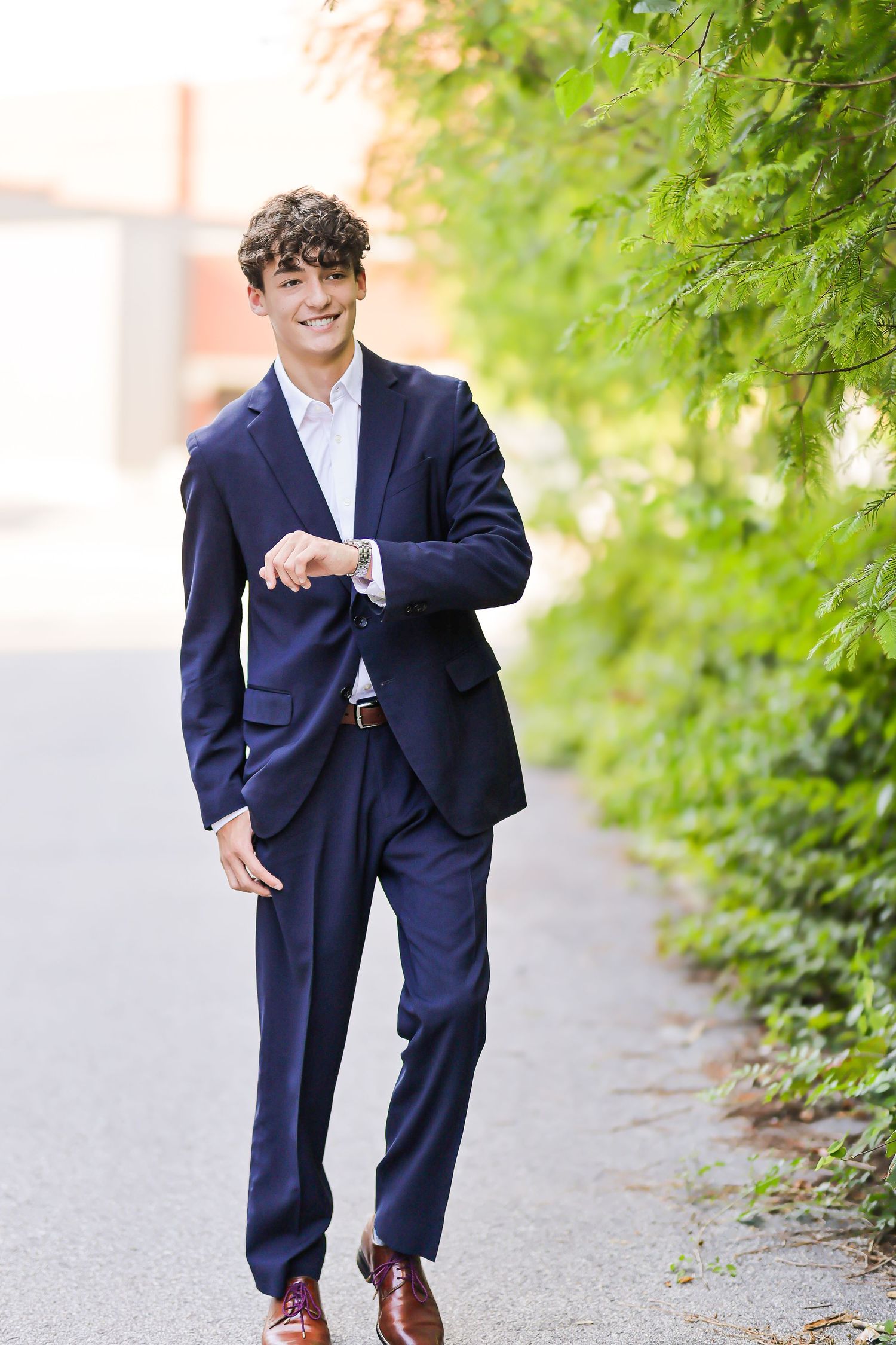 A young child wearing a navy blue suit and brown shoes walks along a tree-lined path outdoors. philadelphia