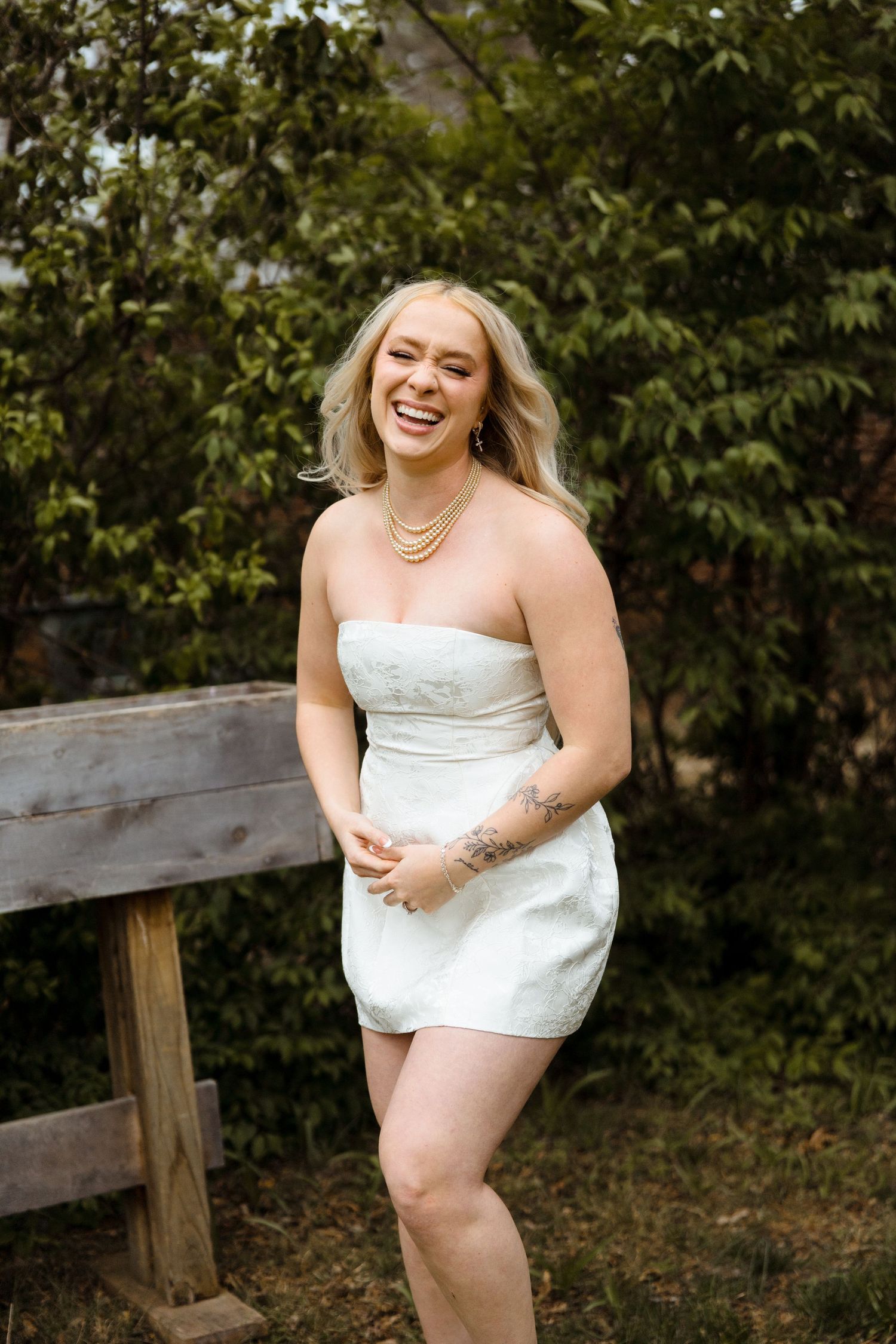 Philadelphia outdoor portrait photos showing someone in a white dress posing playfully against a wooden fence with greenery behind