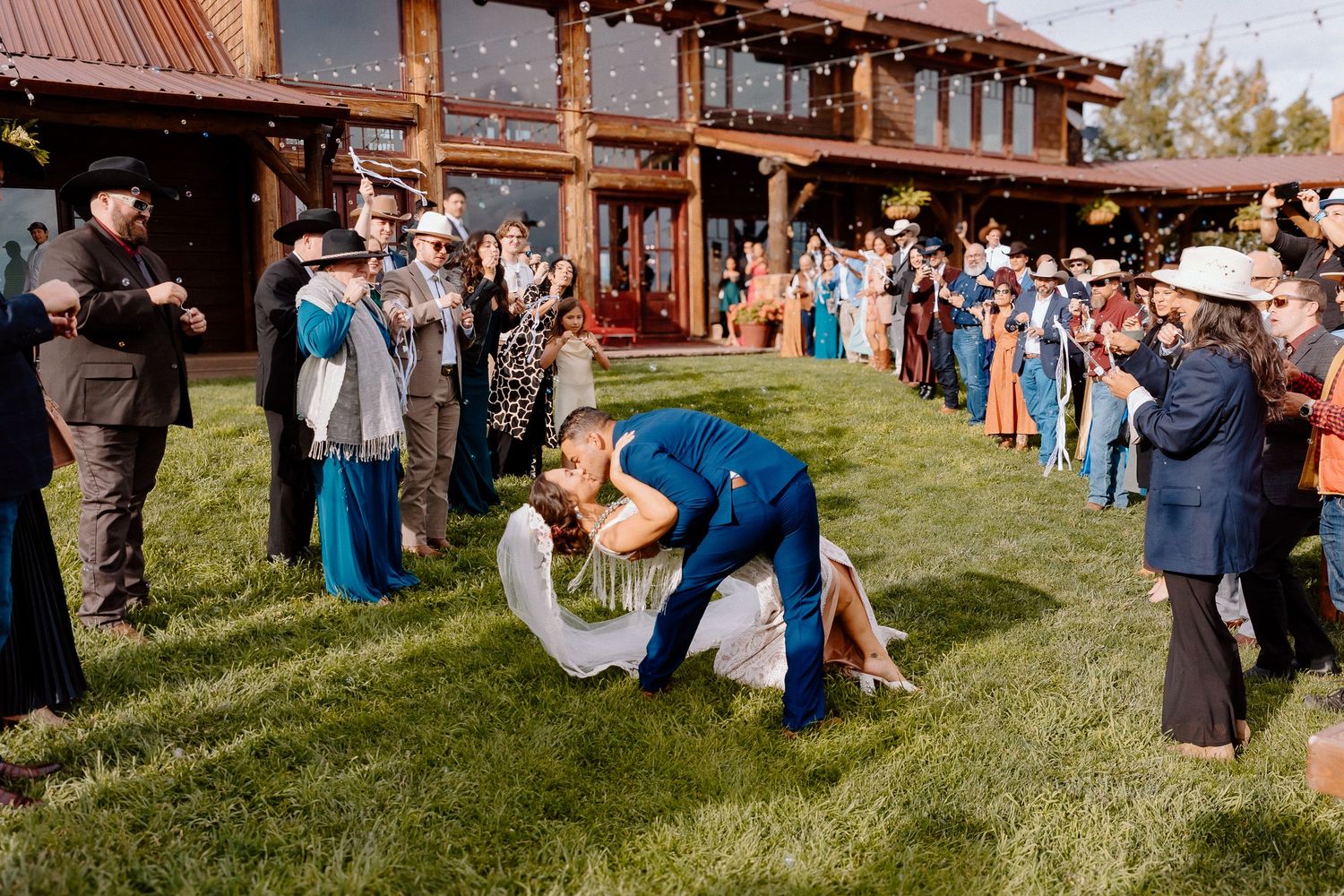 Panoramic view of wedding guests gathered outside rustic wooden venue.