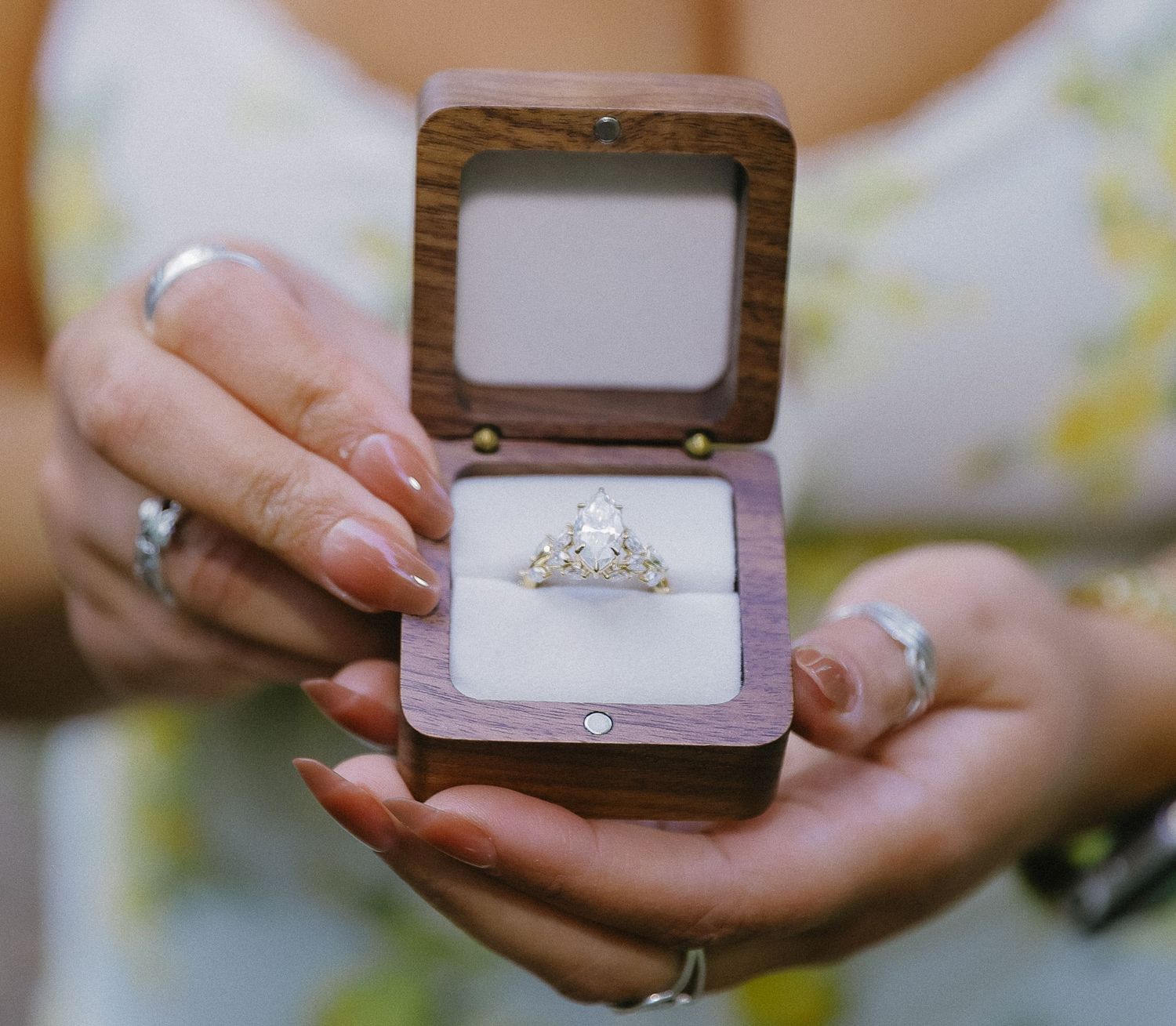 Four close-up shots showing hands holding open ring boxes displaying engagement rings against blurred backgrounds for traveling engagement