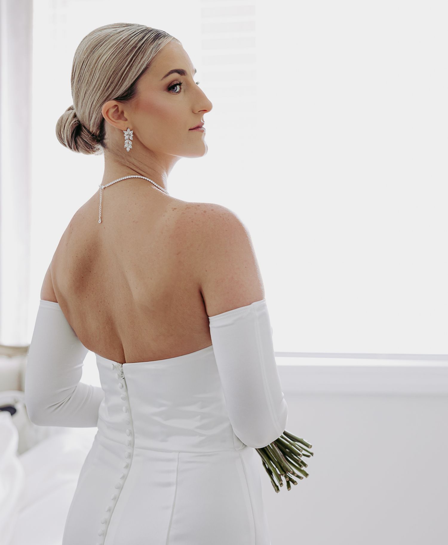 A Philadelphia bride in a sleek white off-shoulder gown poses elegantly in a bright minimalist setting with natural light.