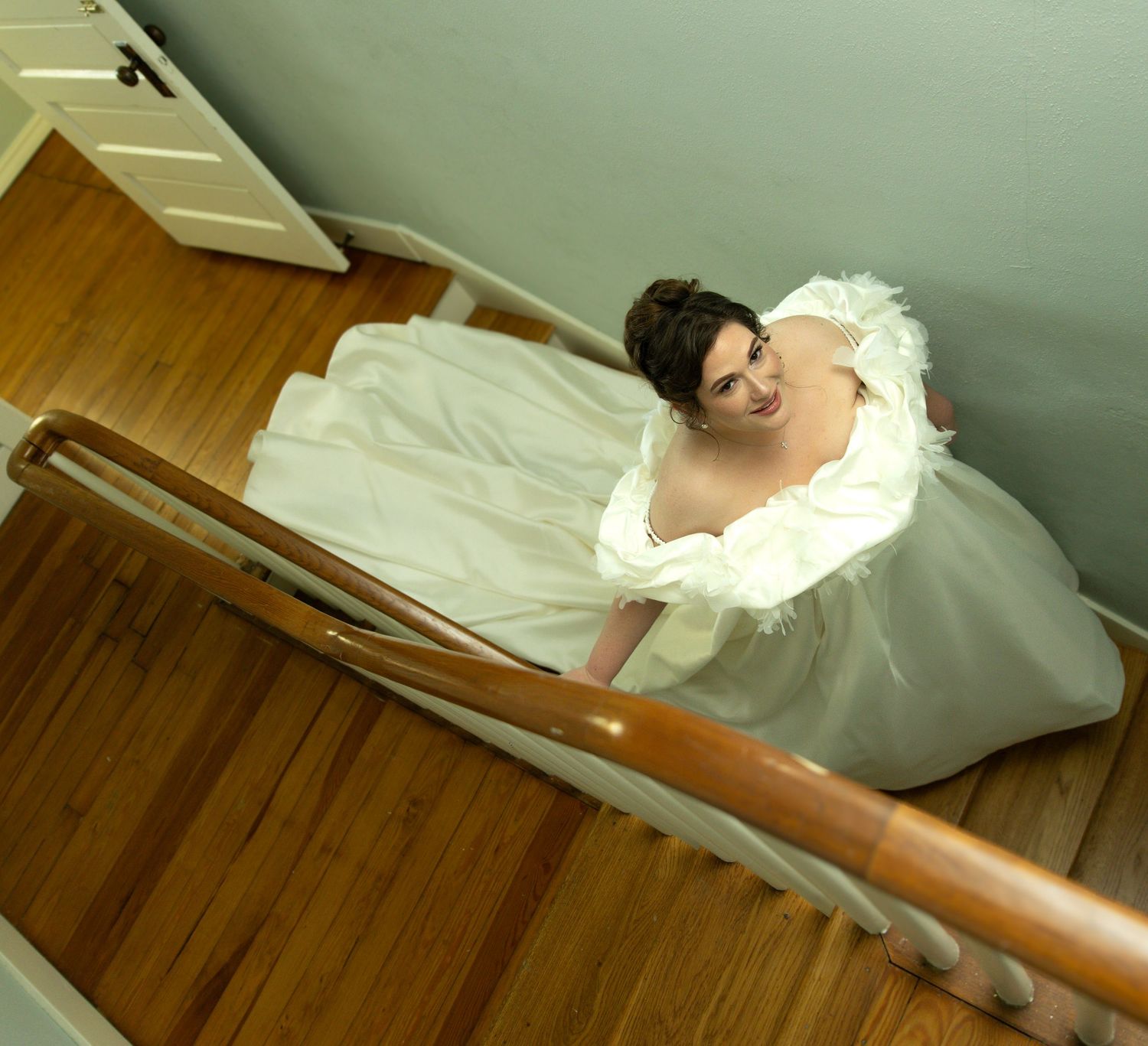 Wedding dress details shown cascading down wooden stairs in dramatic lighting.