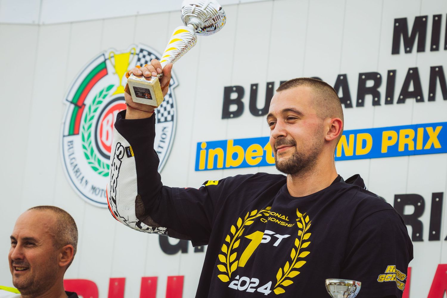 Motorcycle racer holding trophy on podium after race victory – sports photography in Bulgaria.